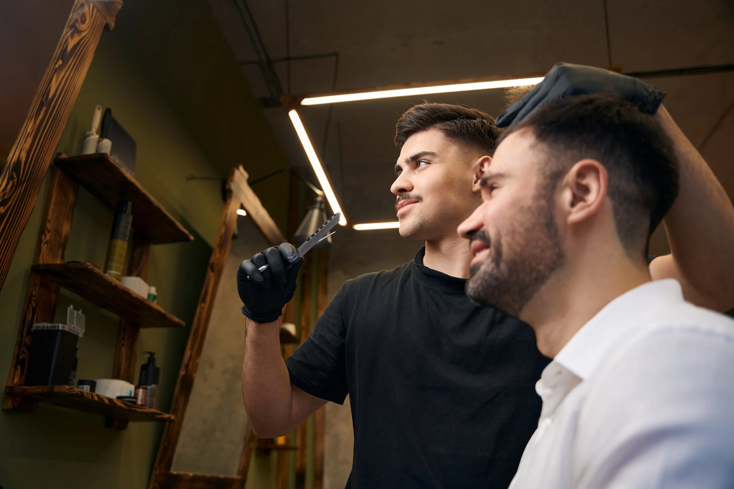 A gloved barber uses clippers as a client checks his fresh fade in the mirror during a men's haircut in Chicago.