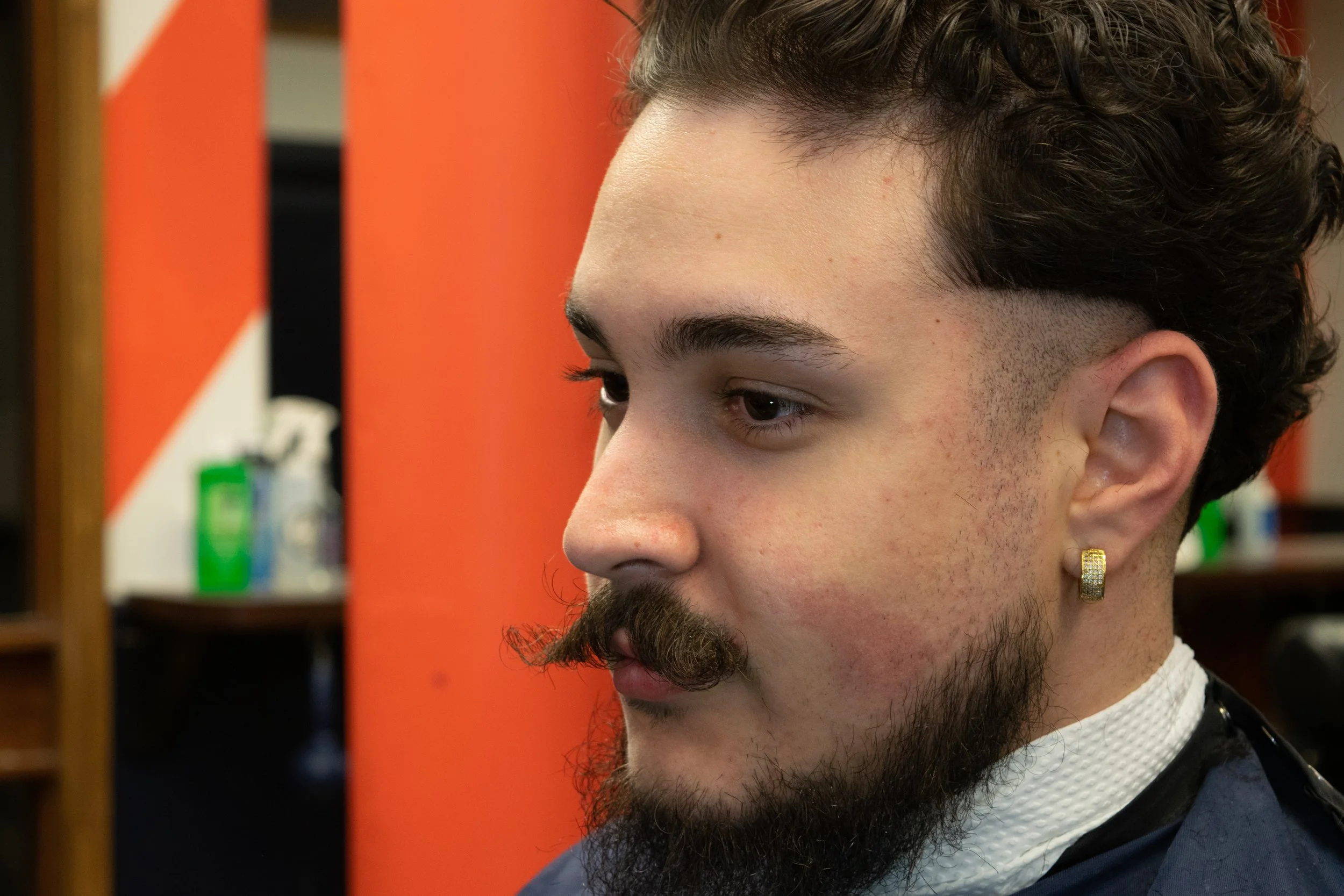 Side profile of a man with textured curls and a high fade at a barbershop.