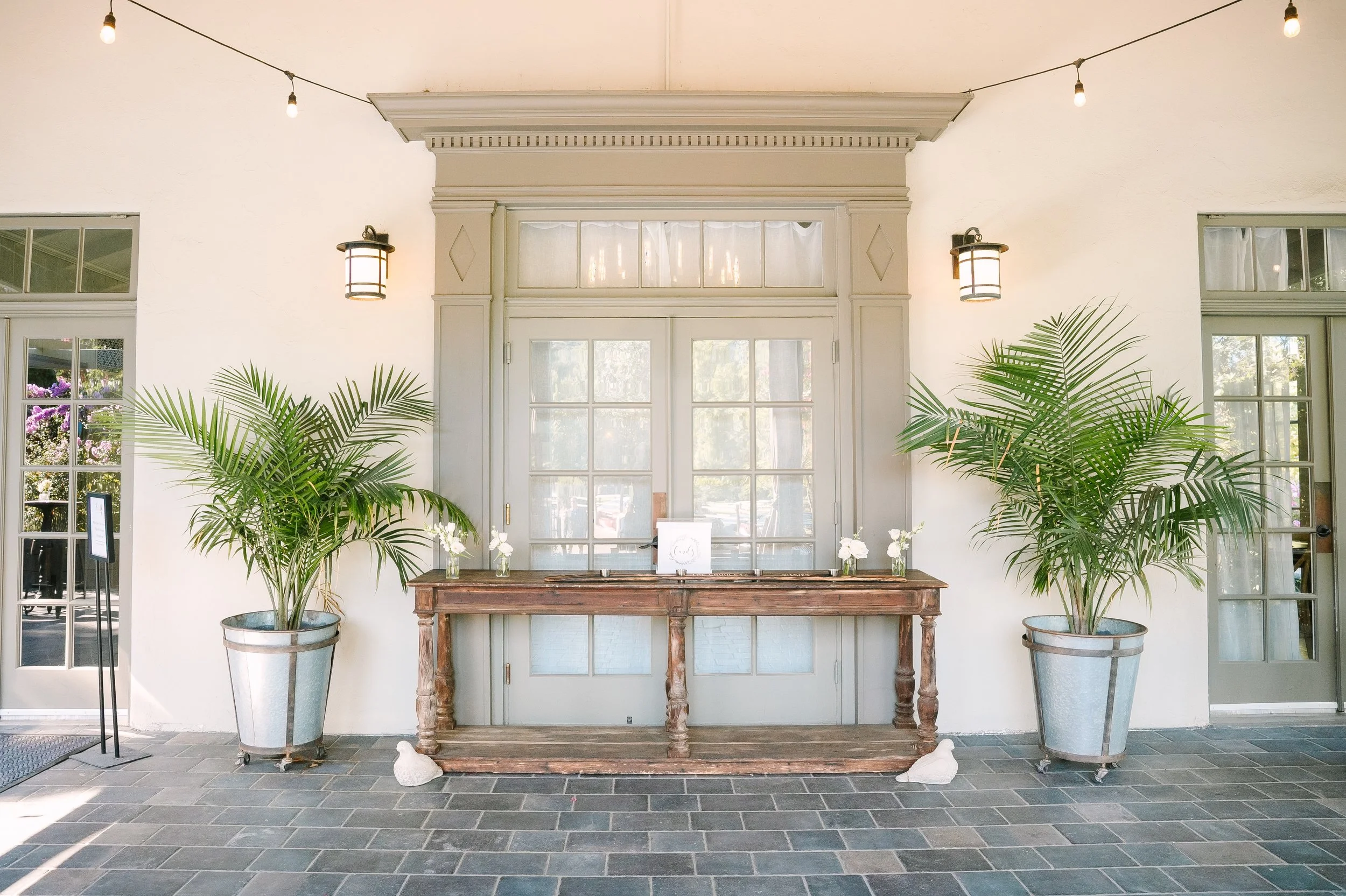 A wood welcome table is set with flowers, on the Front Porch of The Lodge at Malibou Lake wedding venue near Malibou, CA.