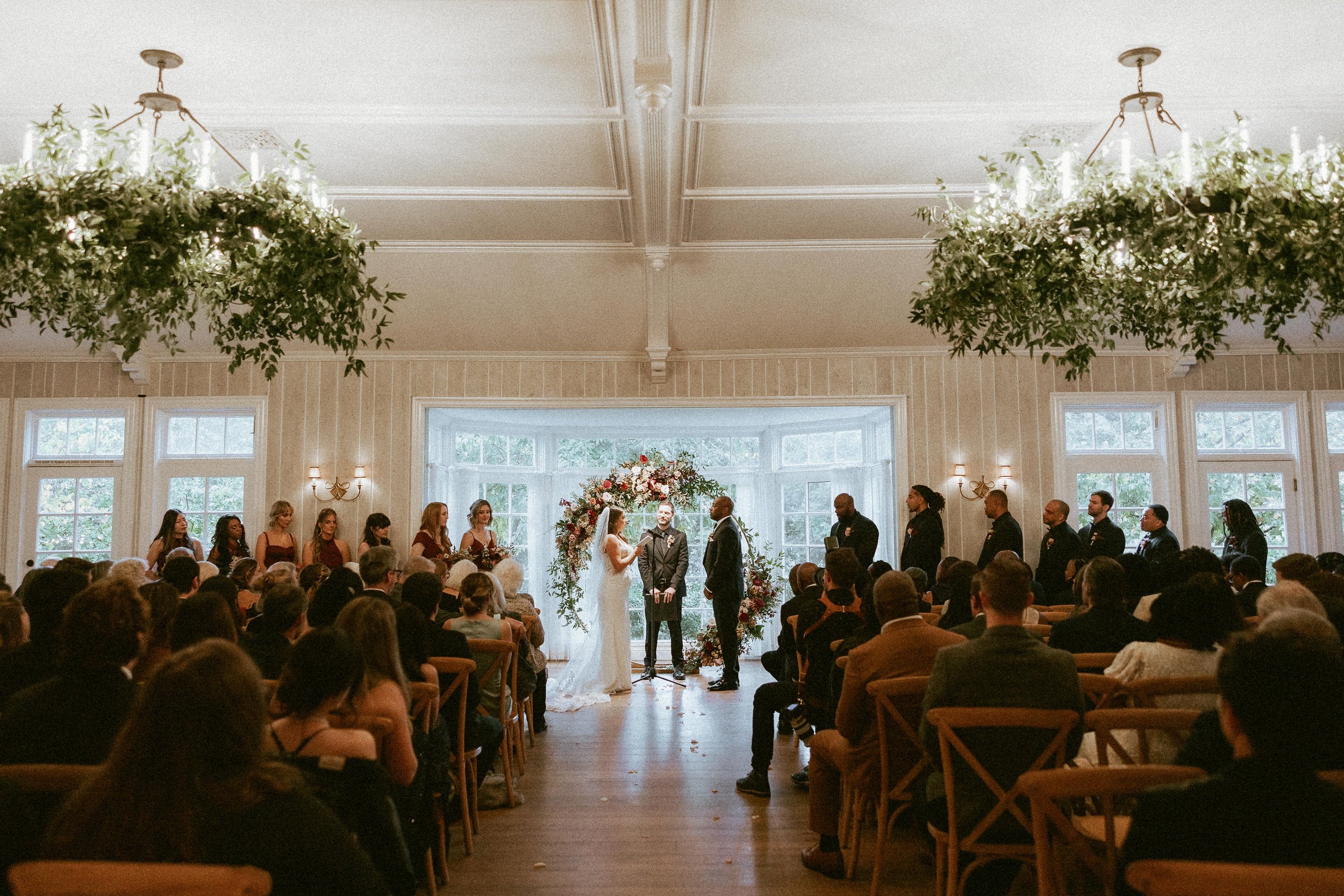 A wedding couple say their vows in a white wood paneled ballroom