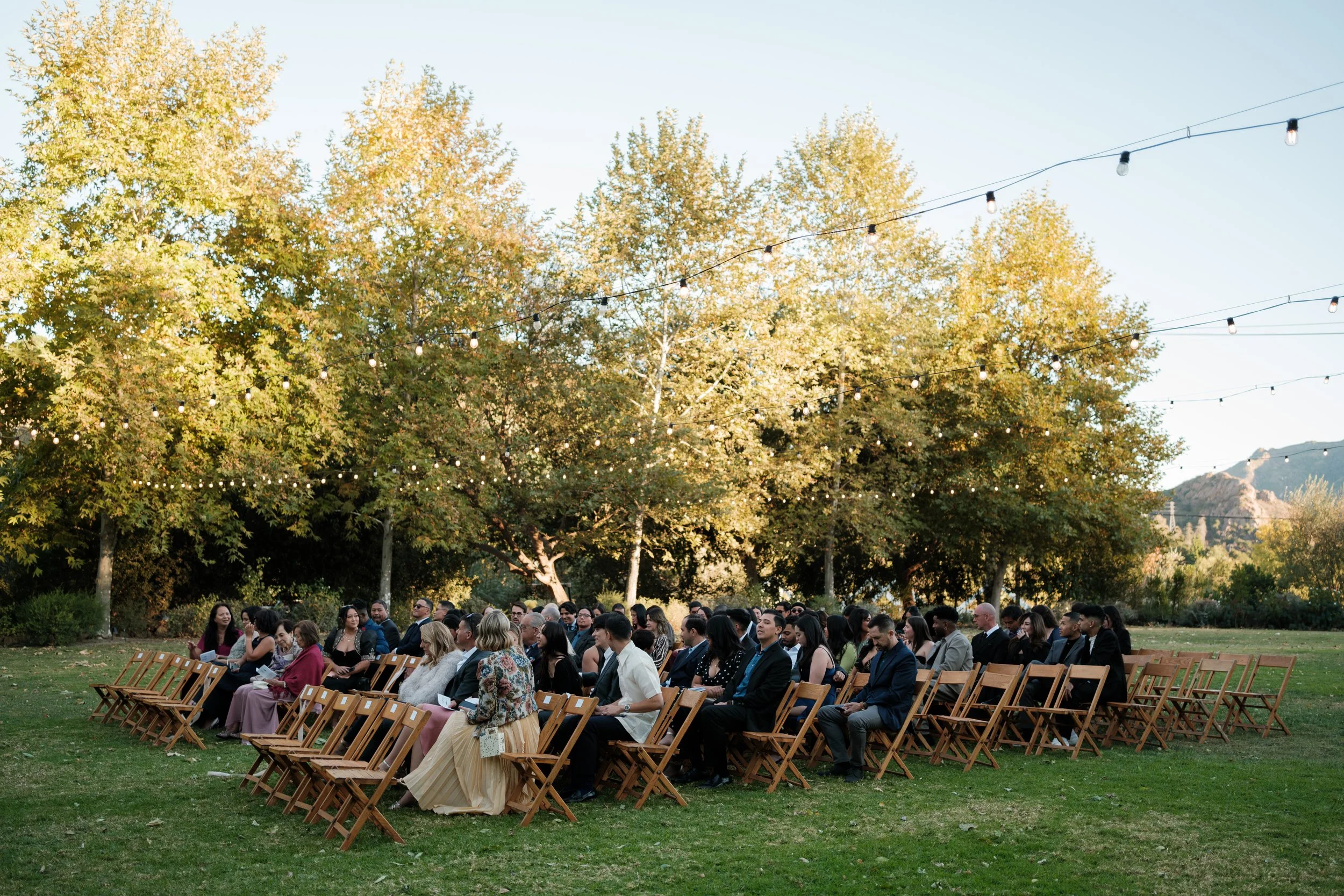 November Wedding: Guests seated at ceremony chairs outdoors on the lawn with the mountains in the distance at The Lodge at Malibou Lake in Agoura Hills CA.