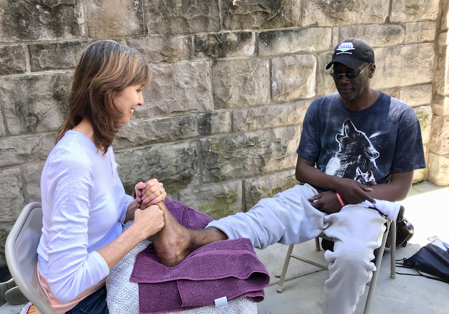 Volunteer massage therapist providing free foot massage to a community member in San Francisco.
