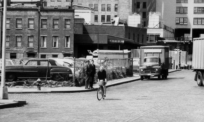 Jane Jacobs cycles past the site of West Village Houses, a low-rise, mixed-income housing development that she championed, in 1962. Getty Images. 