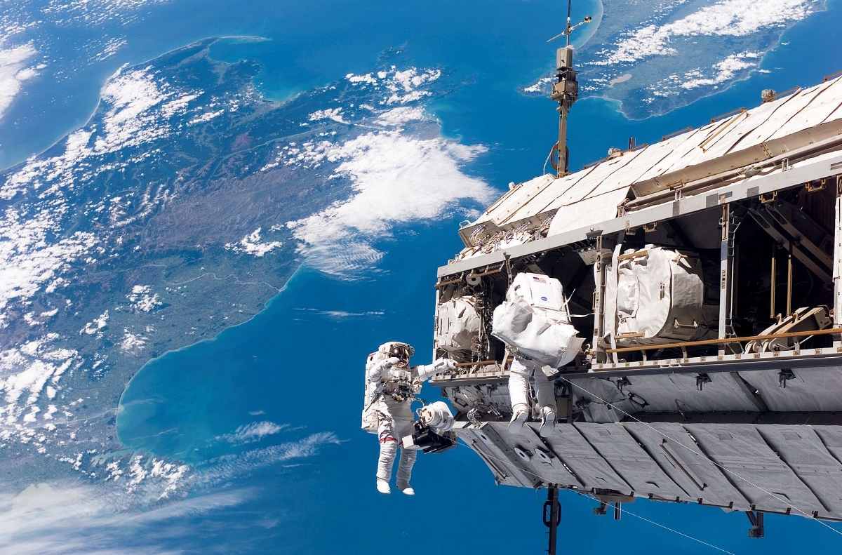 "Backdropped by a colorful Earth, astronaut Robert L. Curbeam, Jr. (left) and European Space Agency (ESA) astronaut Christer Fuglesang, both STS-116 mission specialists, participate in the mission's first of three planned sessions of extravehicular activity (EVA) as construction resumes on the International Space Station. The landmasses depicted are the South Island (left) and North Island (right) of New Zealand."