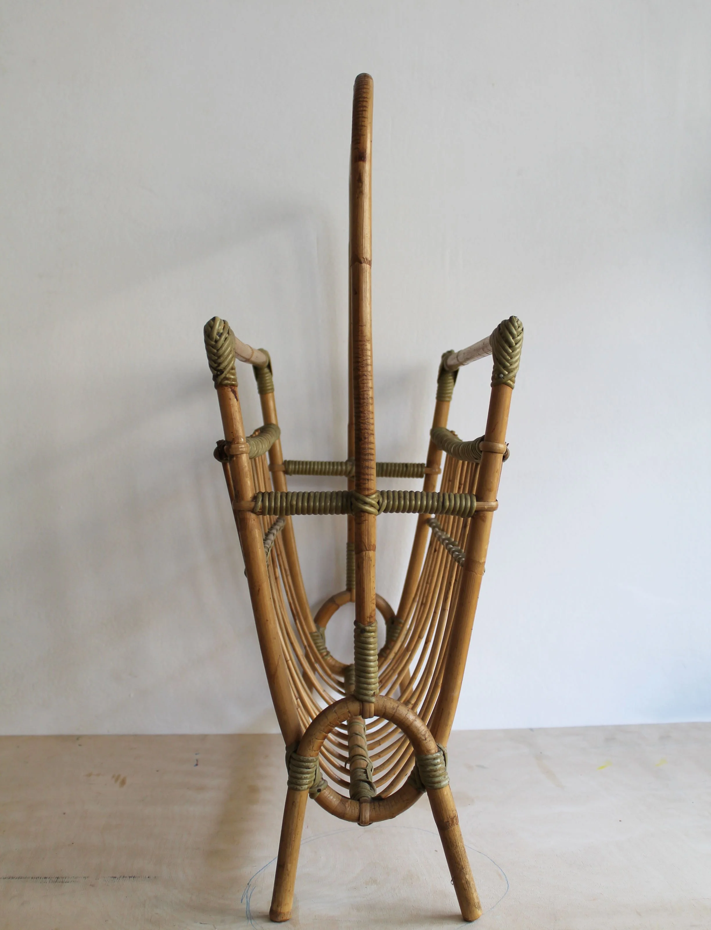 End view of sculptural Czechoslovak rattan magazine rack with circular bent-cane detail and tall central handle
