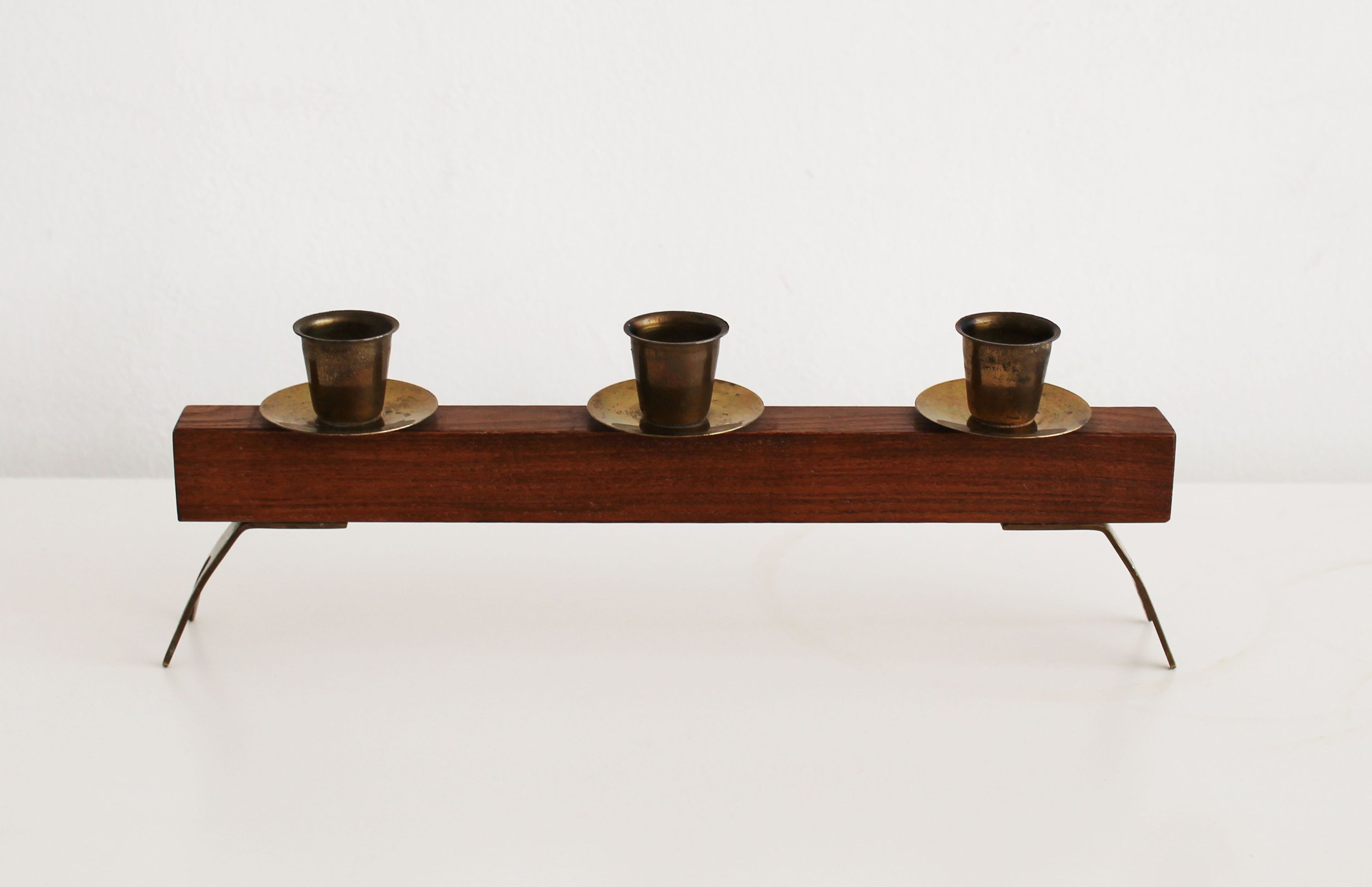 Angled view of sculptural wooden and brass candleholder on white background.