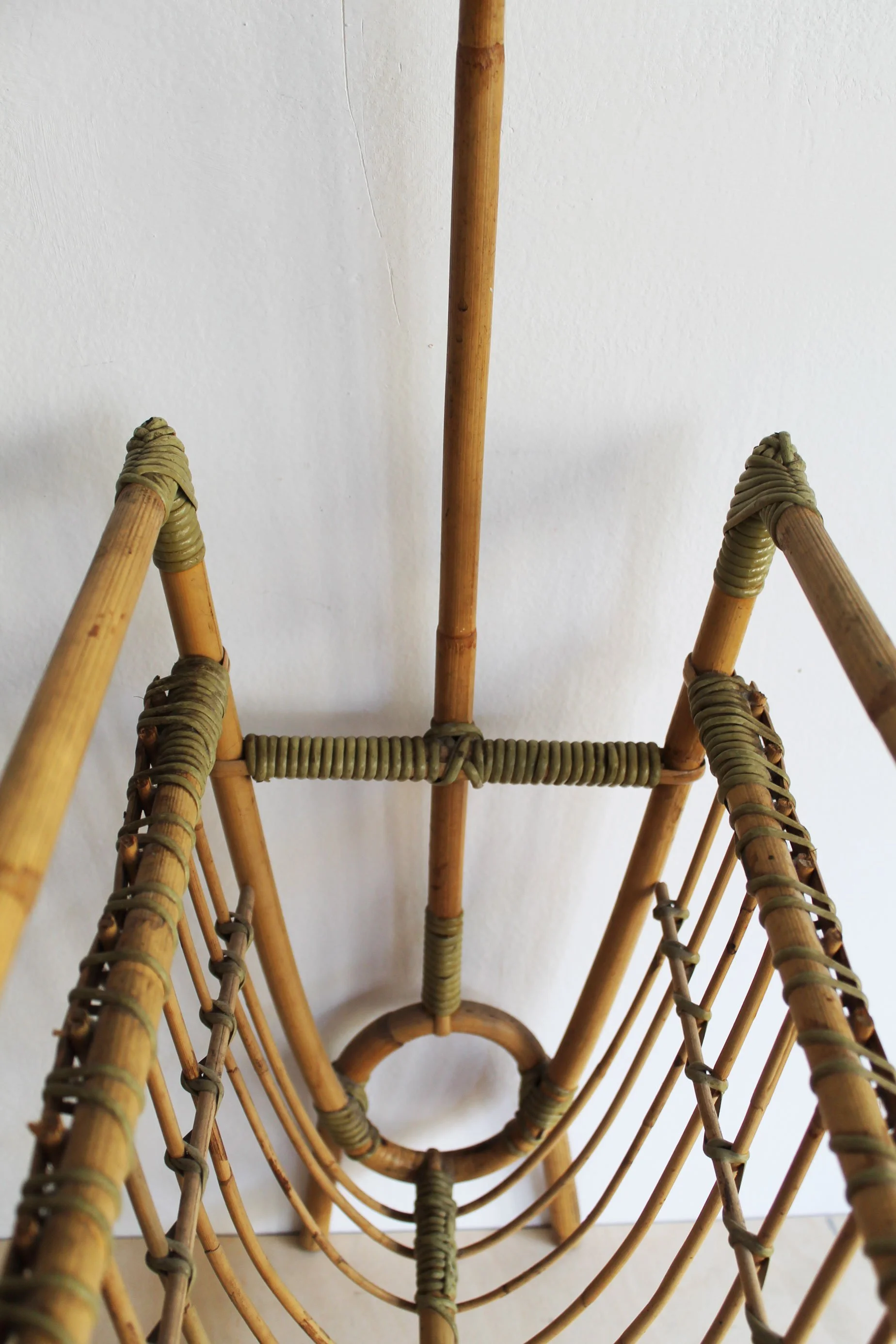 Interior view of rattan magazine rack showing slender curved cane rods forming the two deep storage compartments