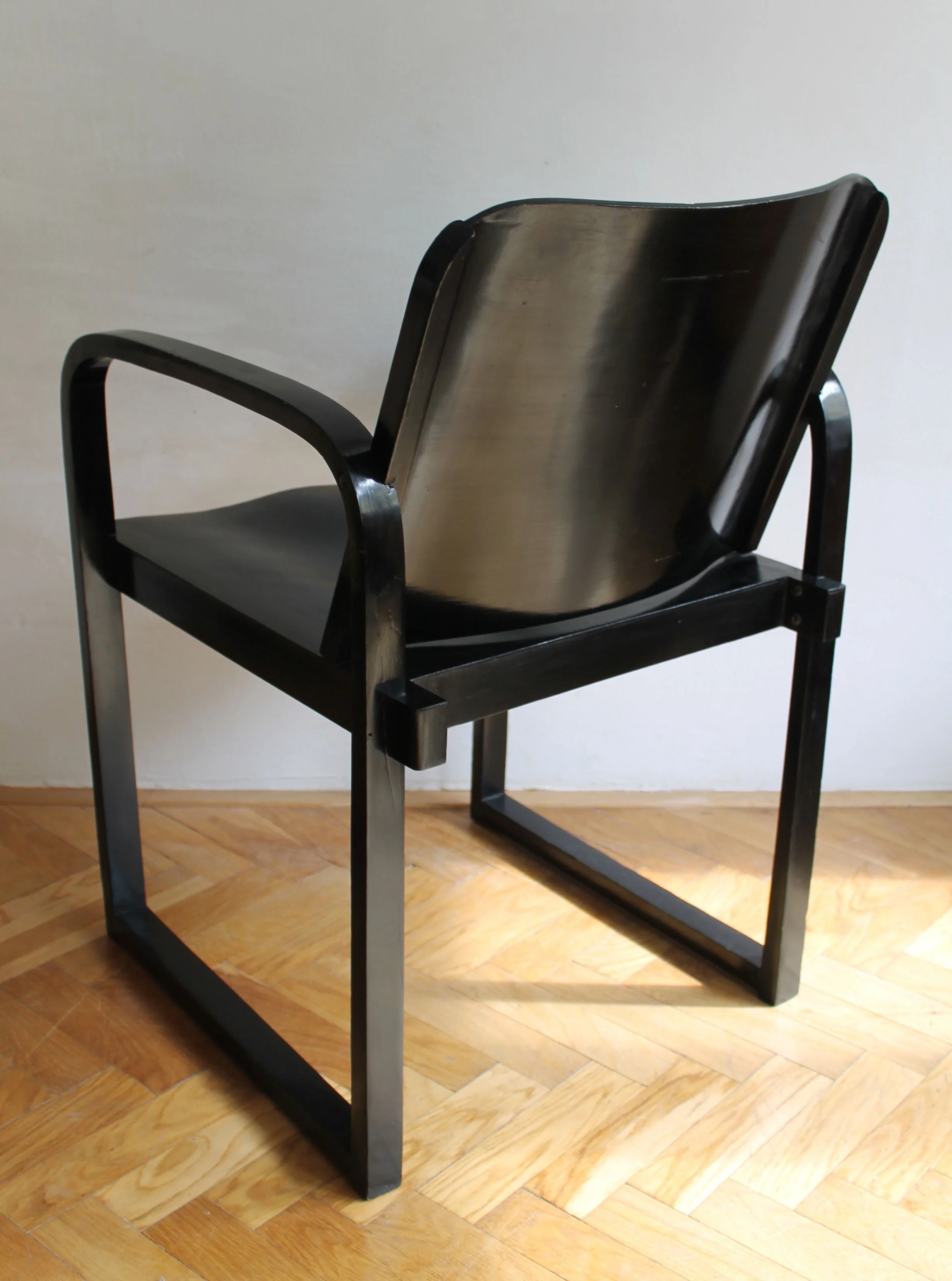 Detail of the broad curved backrest and wooden side supports on the unidentified armchair