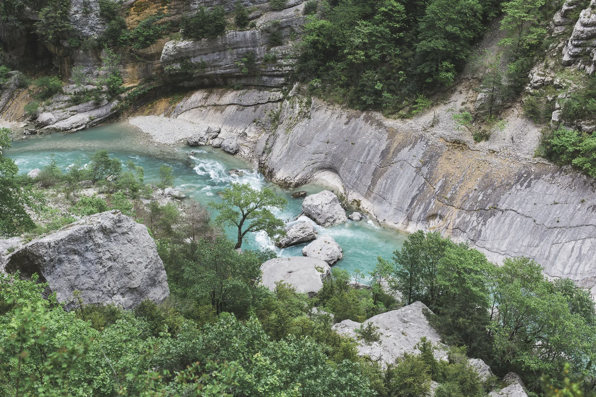 A turquoise river flows through a rocky canyon surrounded by lush green trees and steep gray cliffs.