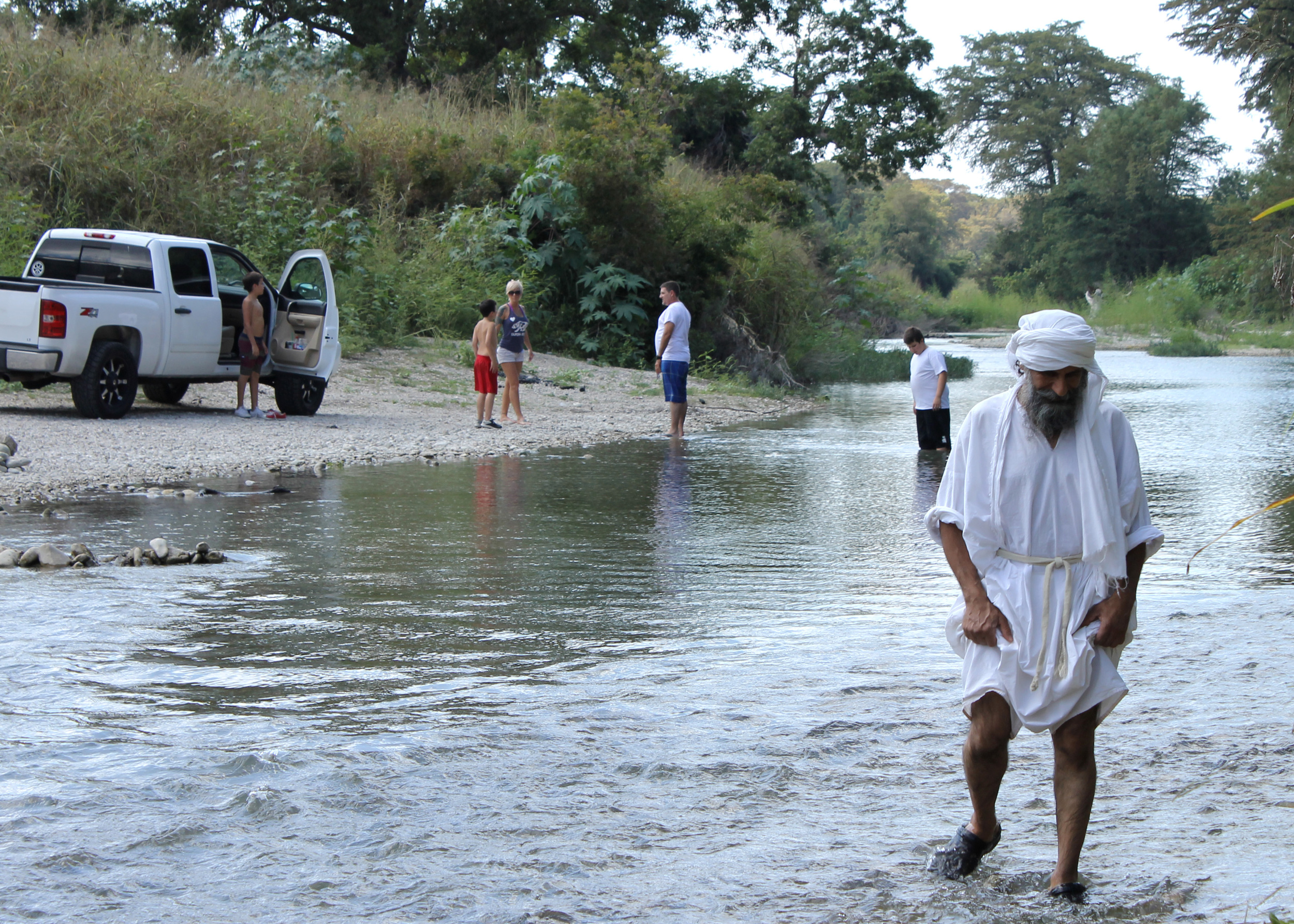 A local family pulls up next to the baptism site to go for a swim as Shahram Ebadfardzadeh wades toward the baptism site. The Mandaeans are sometimes harassed during their ceremonies by local Texans who assume they are Muslim. This family only stared curiously. 