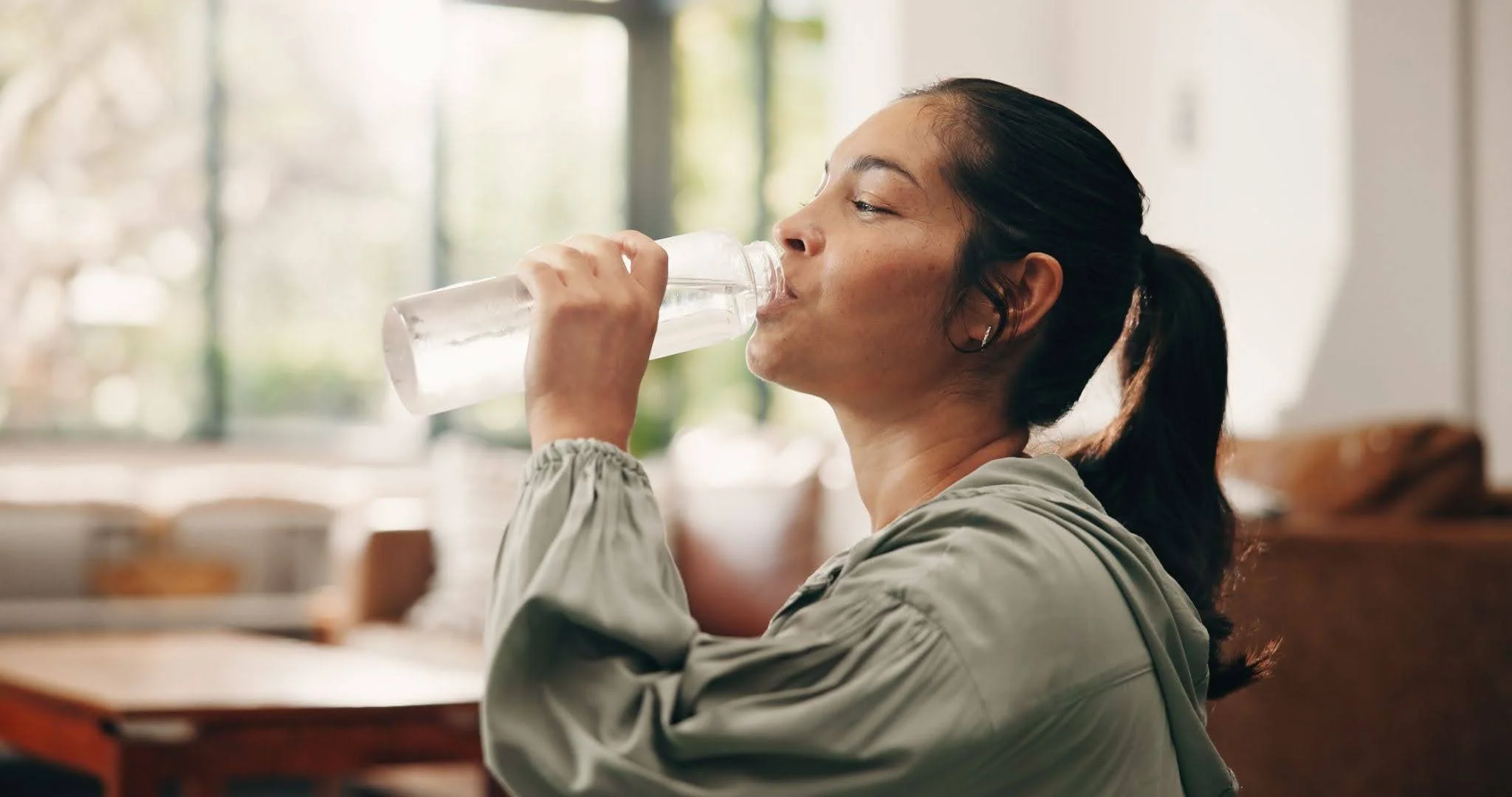 A young girl drinking water from a transparent water bottle
