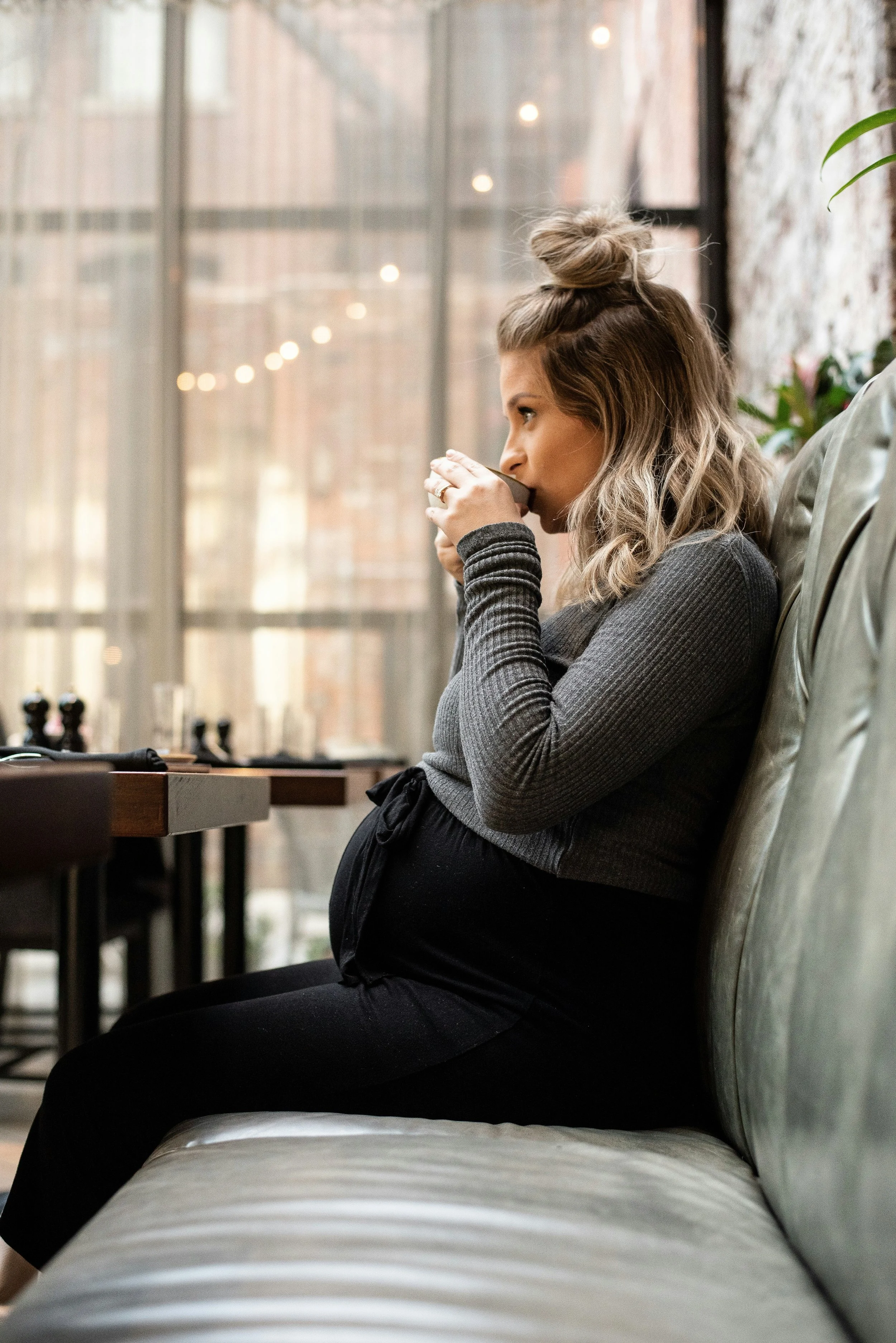 a pregnant woman sipping a hot drink on a sofa