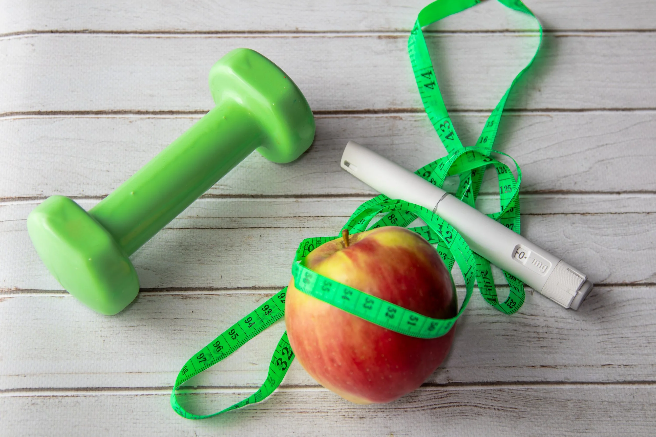 health lifestyle concept with an apple, dumbbell, injection pen, and a measuring tape