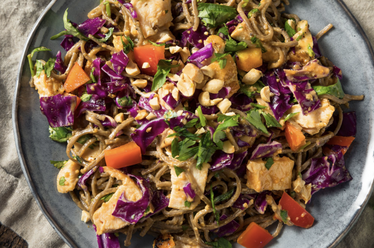 a plate of chicken noodle with chicken and peanuts