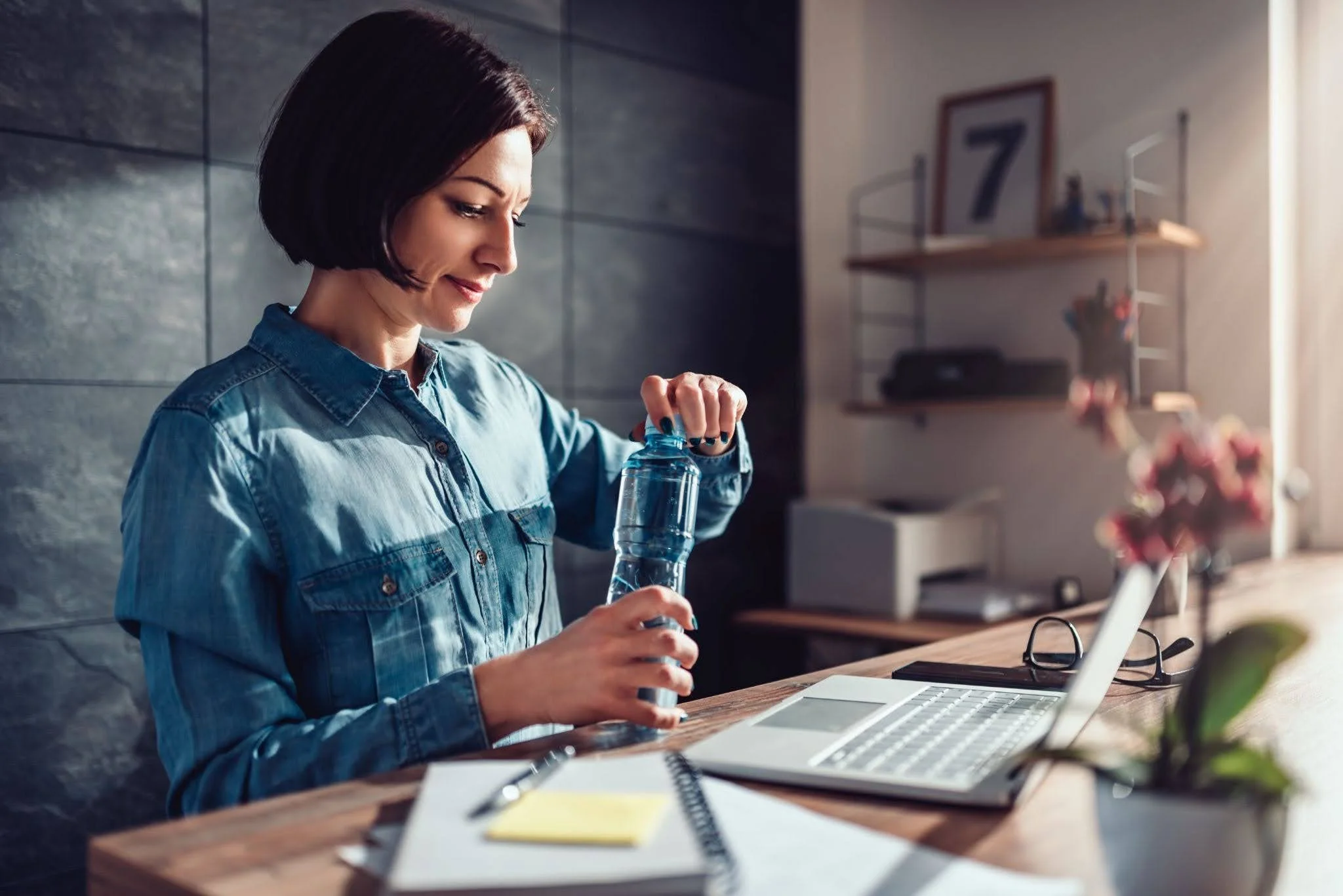 A young woman opening a bottle of water while working at a desk