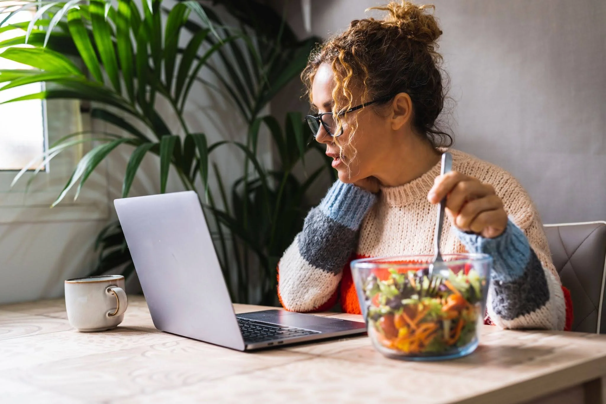 a woman eating a salad from a glass bowl while working at her desk