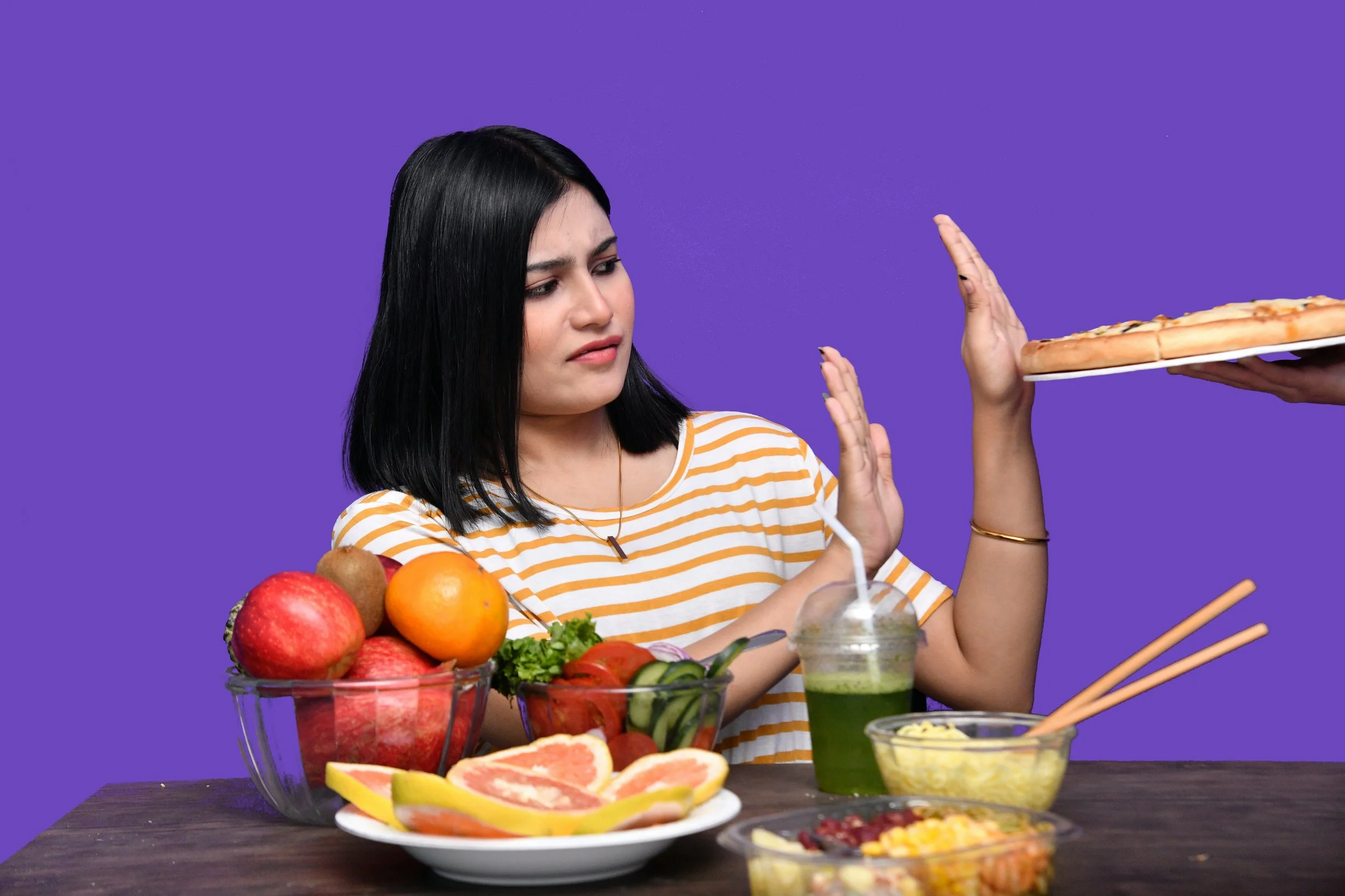 a woman at the table full of fruit rejecting pizza