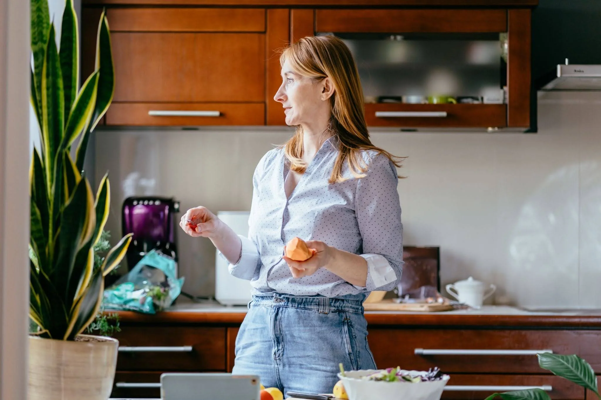 a woman in her 50s holding a vegetable and thinking about what to cook to reduce food noise