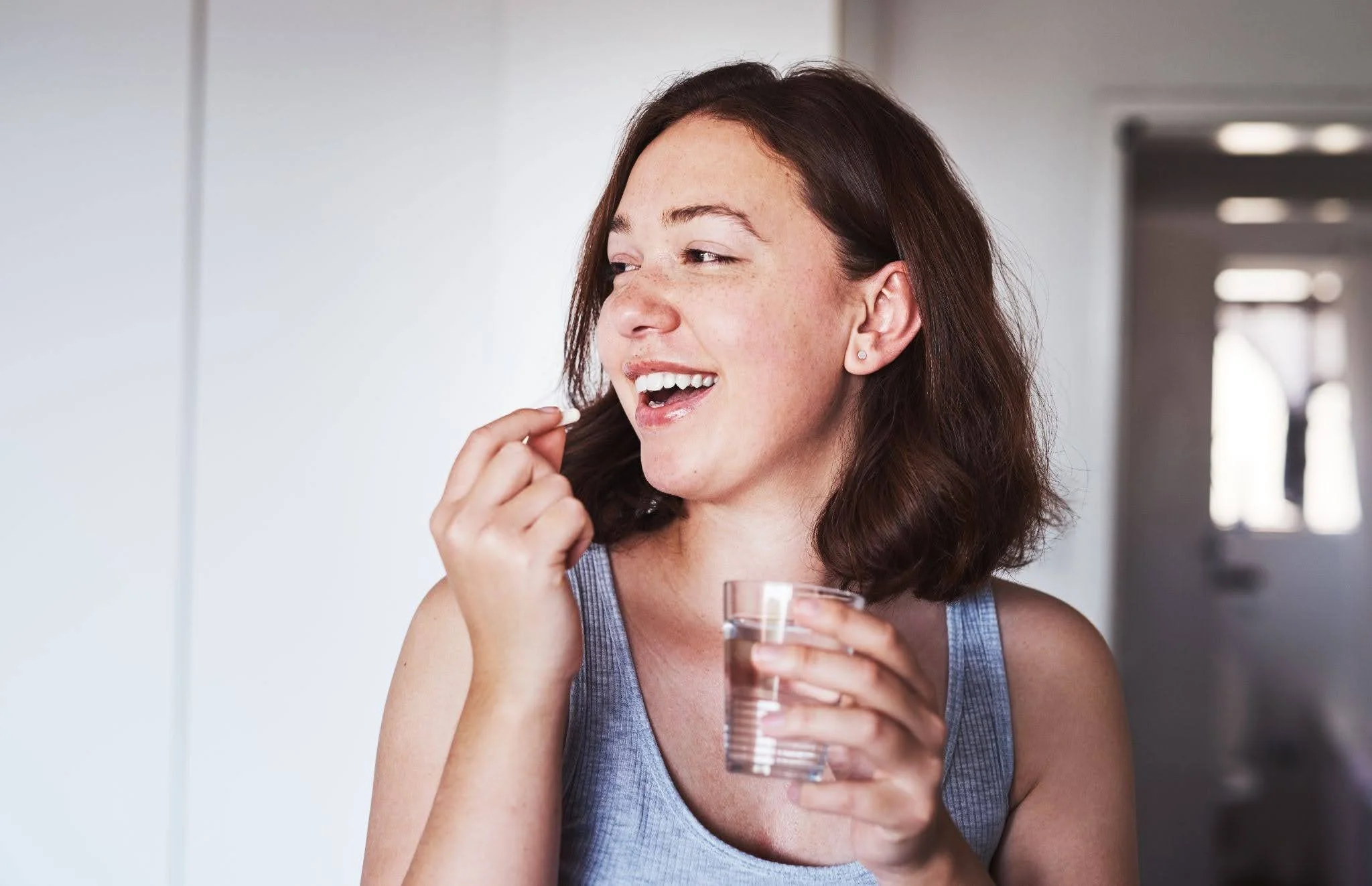 a smiling woman drinking a pill with a glass of water