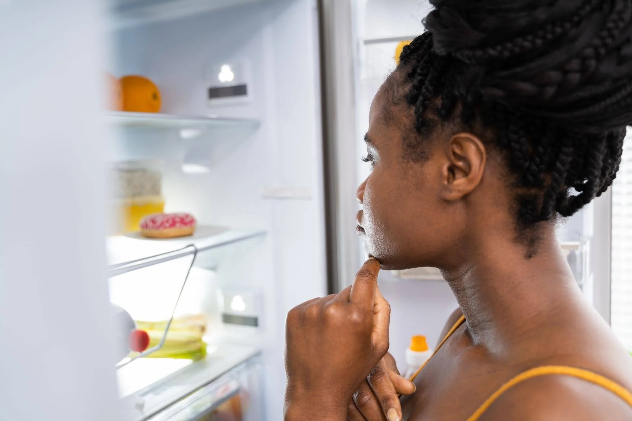 an African woman looking into her fridge and thinking what to eat