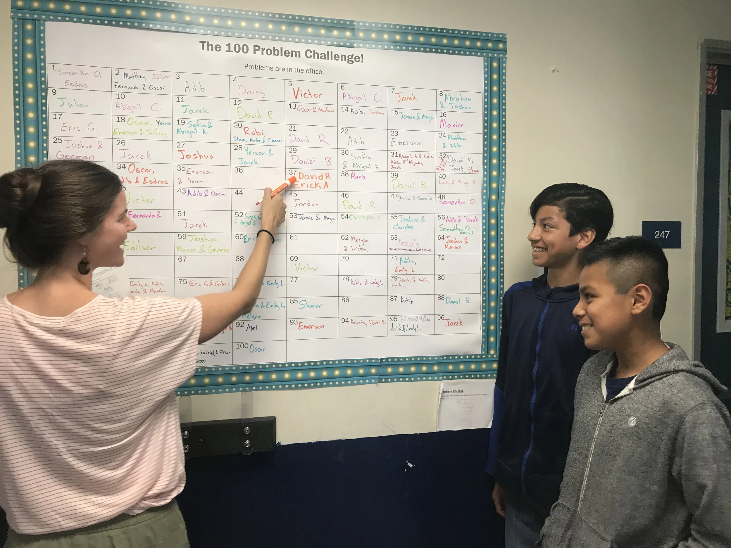 David (right) and Erick A. (middle) solved one of the challenge problems, so Meghan (left) writes their names on the poster.