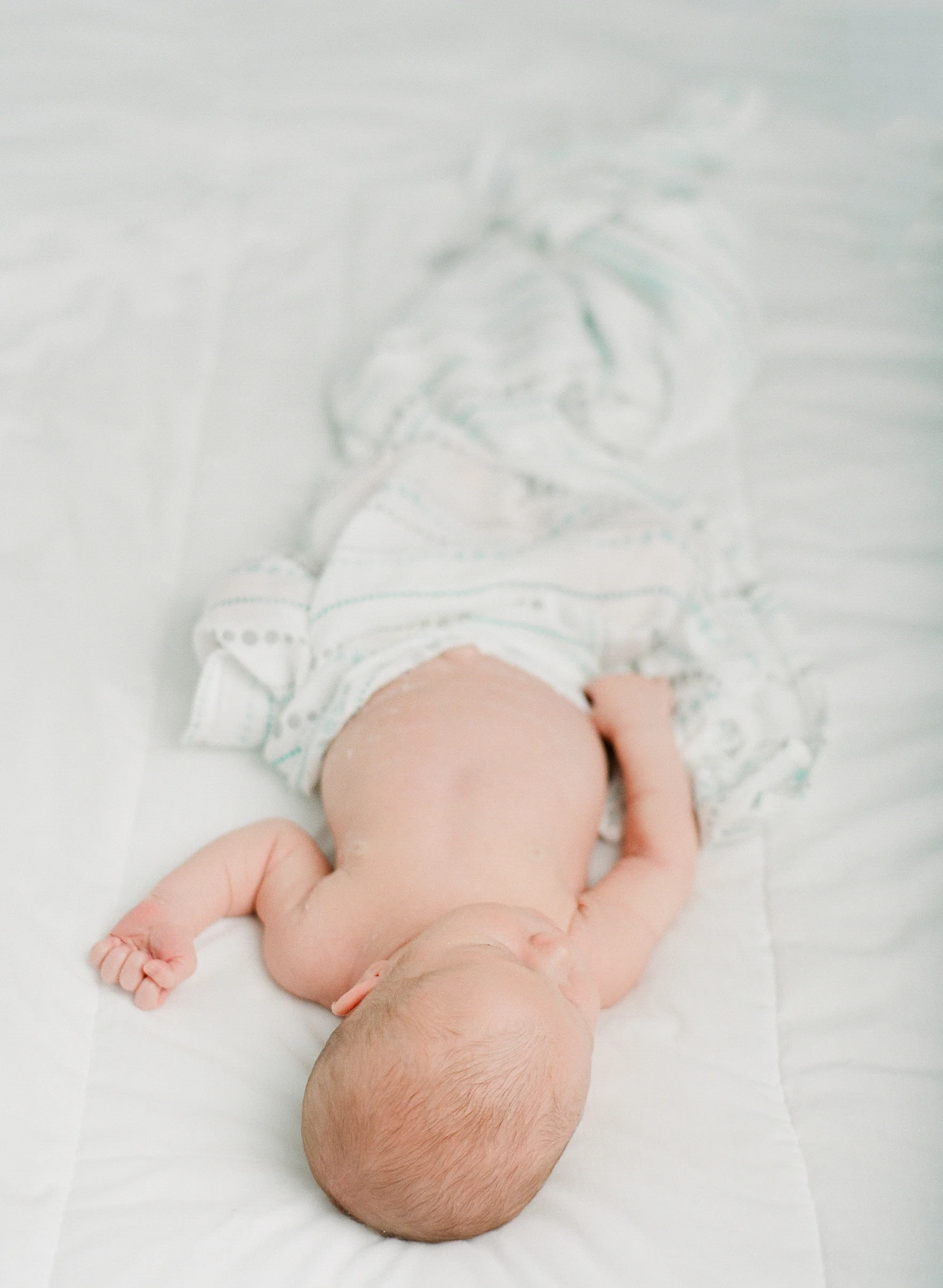 Newborn photography Seattle, by Sandra Coan. Studio photograph. Newborn swaddled and sleeping on a white bed.