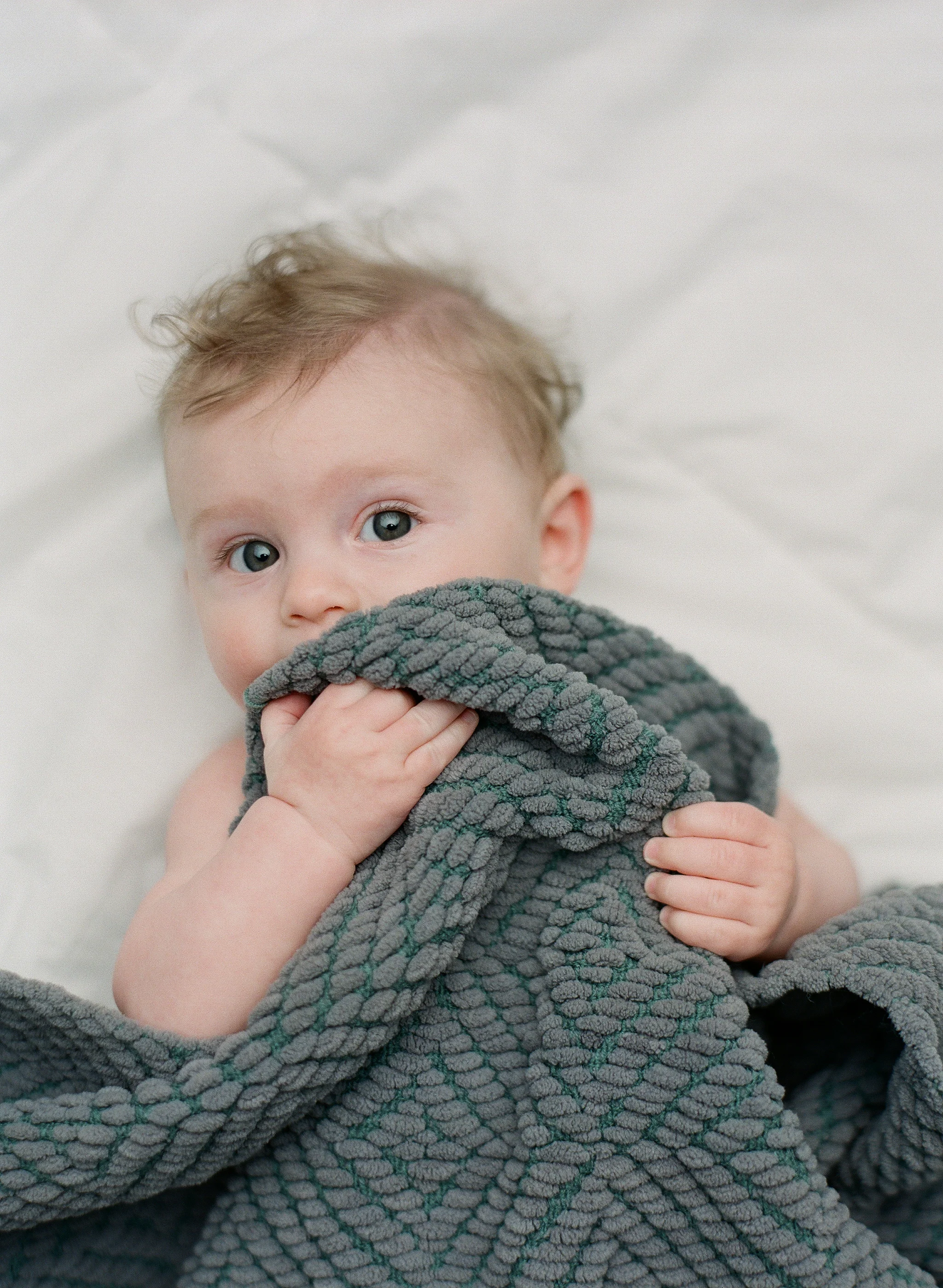 Newborn photography Seattle, by Sandra Coan. Studio photograph. Baby peaking up from under a blanket.