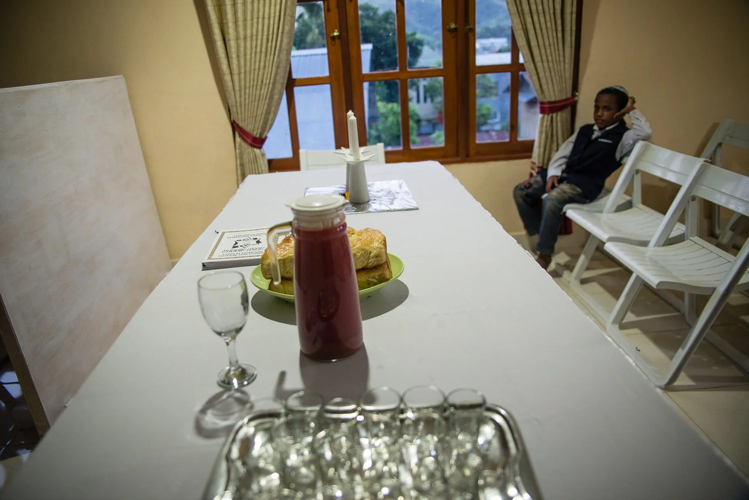 A young member waits for Friday night Shabbat services to begin. The grape juice set on the table is homemade by Harun or Diane every week, and the children get especially excited for a sweet treat.