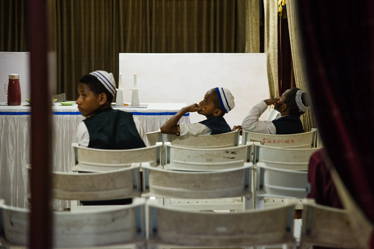 Annis, Charlie Kecil (little Charlie), and Hosea wait for Friday night Shabbat services to begin. The community wears their best clothes for Shabbat, including the children.