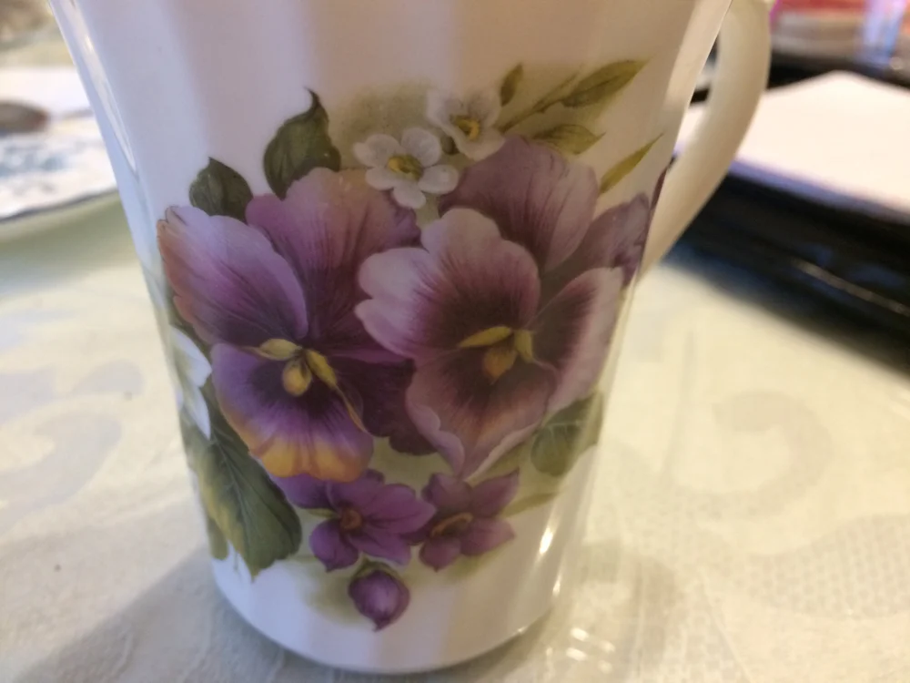 Purple pansies hand-painted on the side of a ceramic tea cup.