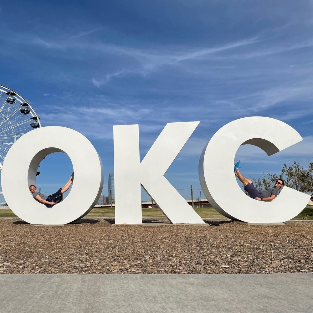 Two people pose in an art installation the spells out OKC.