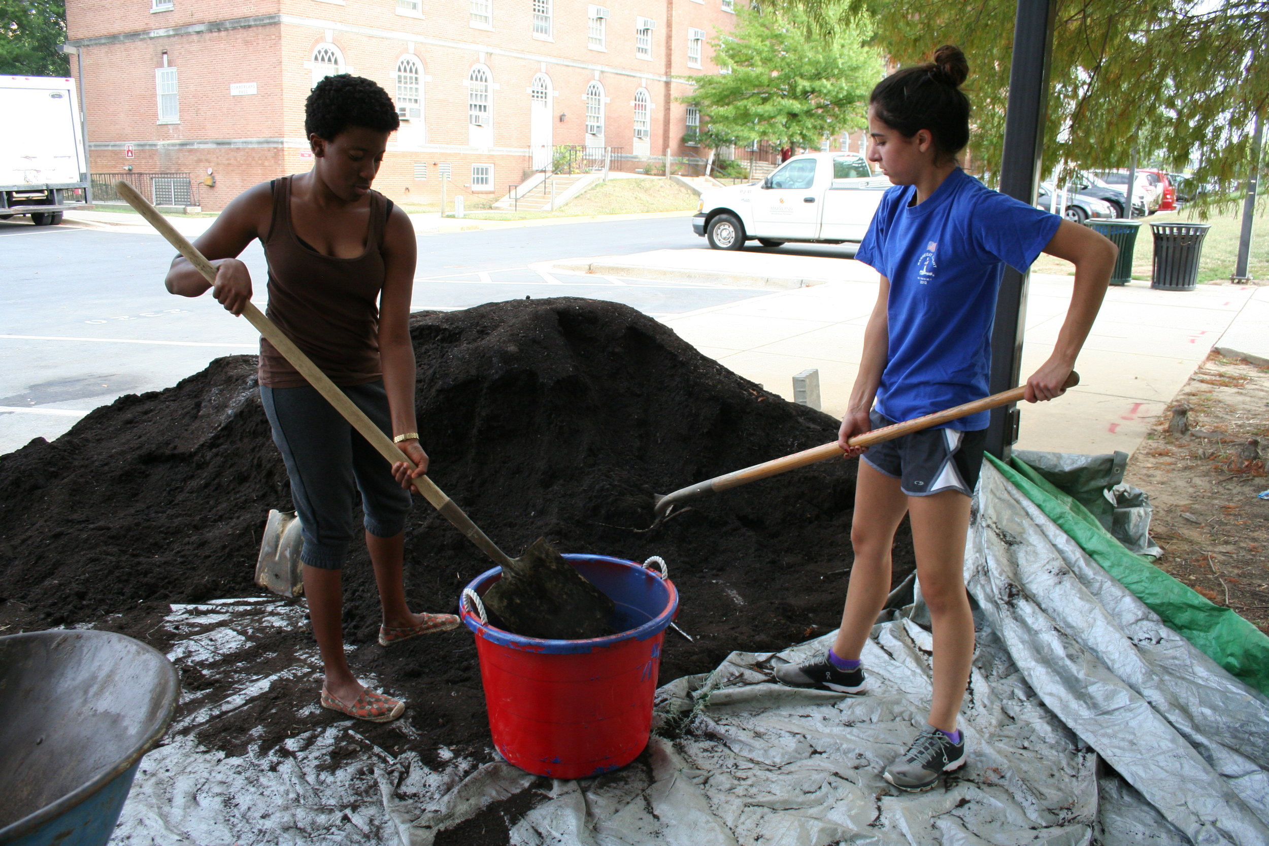  Asamaniwa Padi-Adjirackor, left, &nbsp;a sophomore agriculture and resource economics major and Claudia Romeo, right, a freshman elementary education major, begin their work hour at the Public Health Garden by shoveling and transporting compost prov