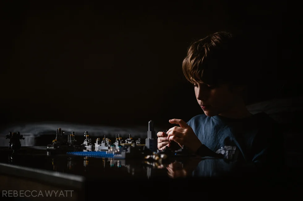color photograph of boy side lit dramatically while playing legos