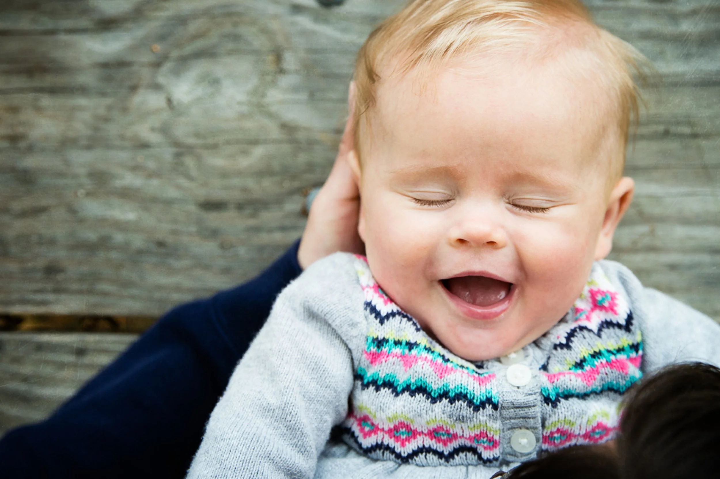 baby girl laughing with in her dad's arms on a picnic table.