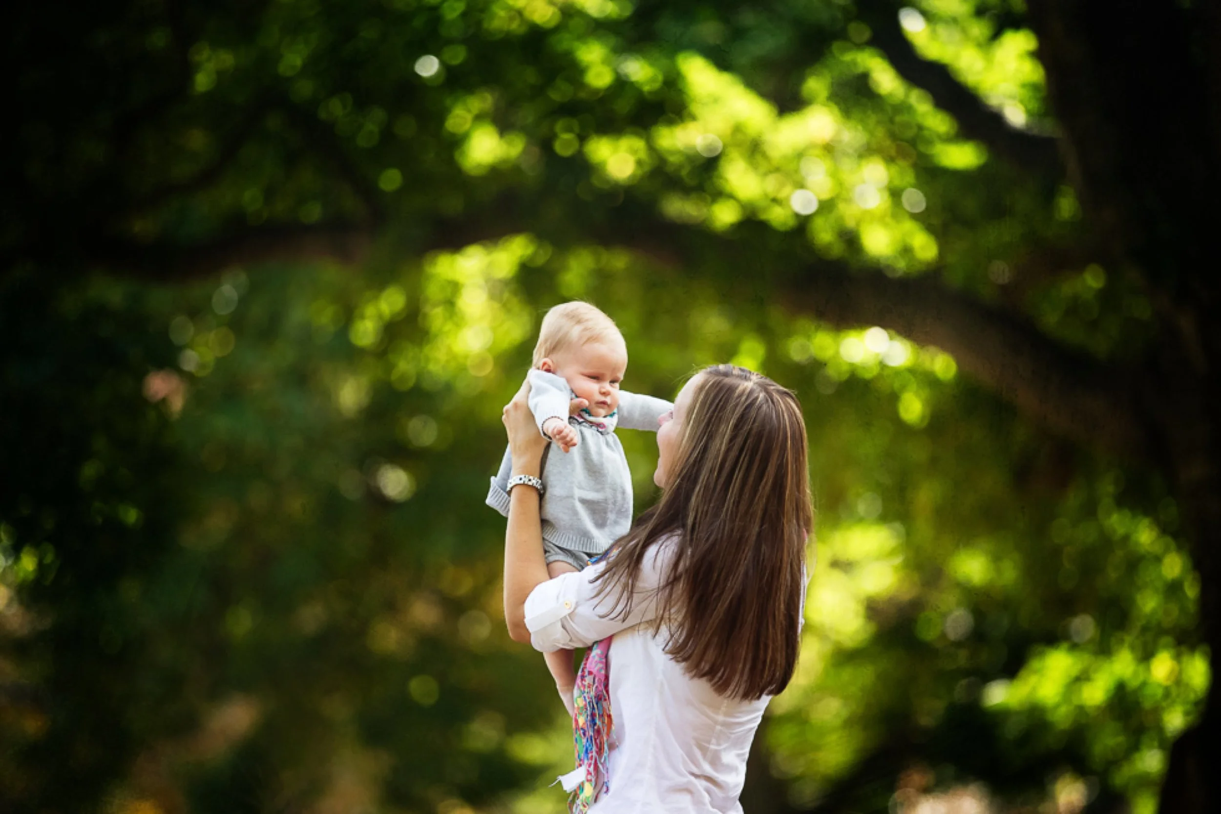 baby being held in the air looking at her mom in a Baltimore park.