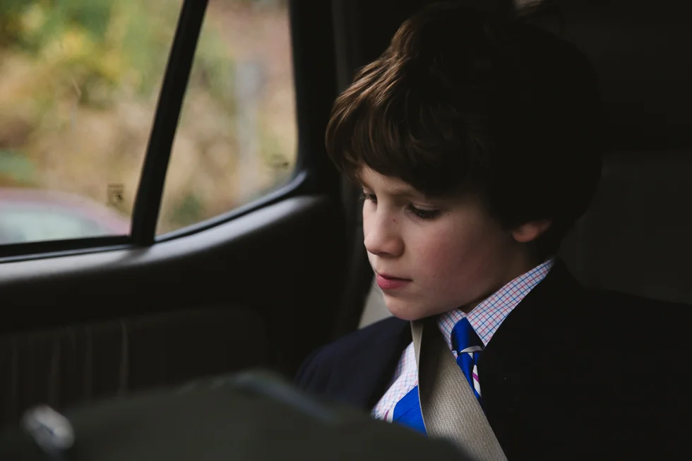 middle school boy in jacket and tie reading in back seat of the car