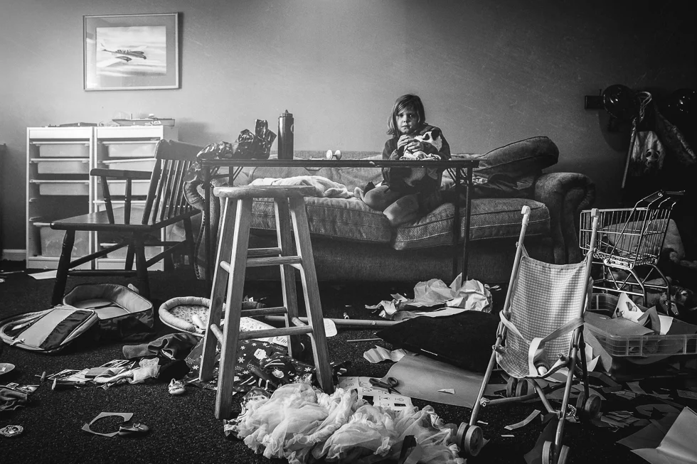 girl sitting in very messy playroom in a black and white photograph