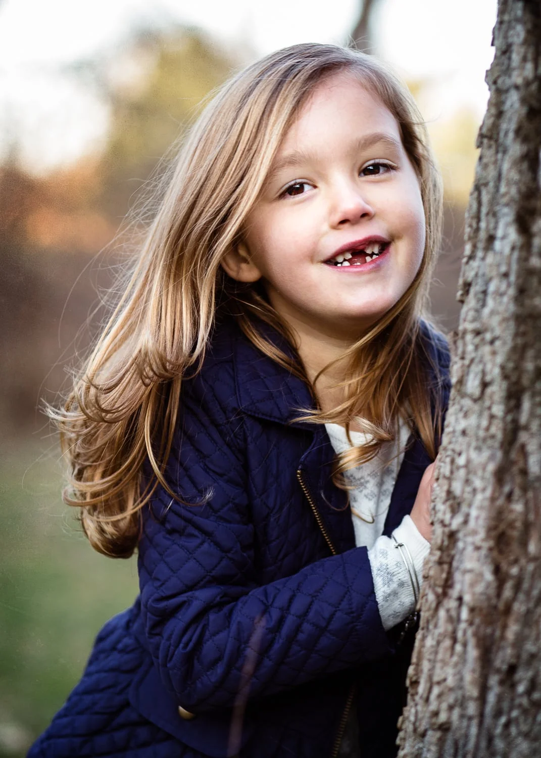Sweet brunette girl smiling at camera next to a tree.