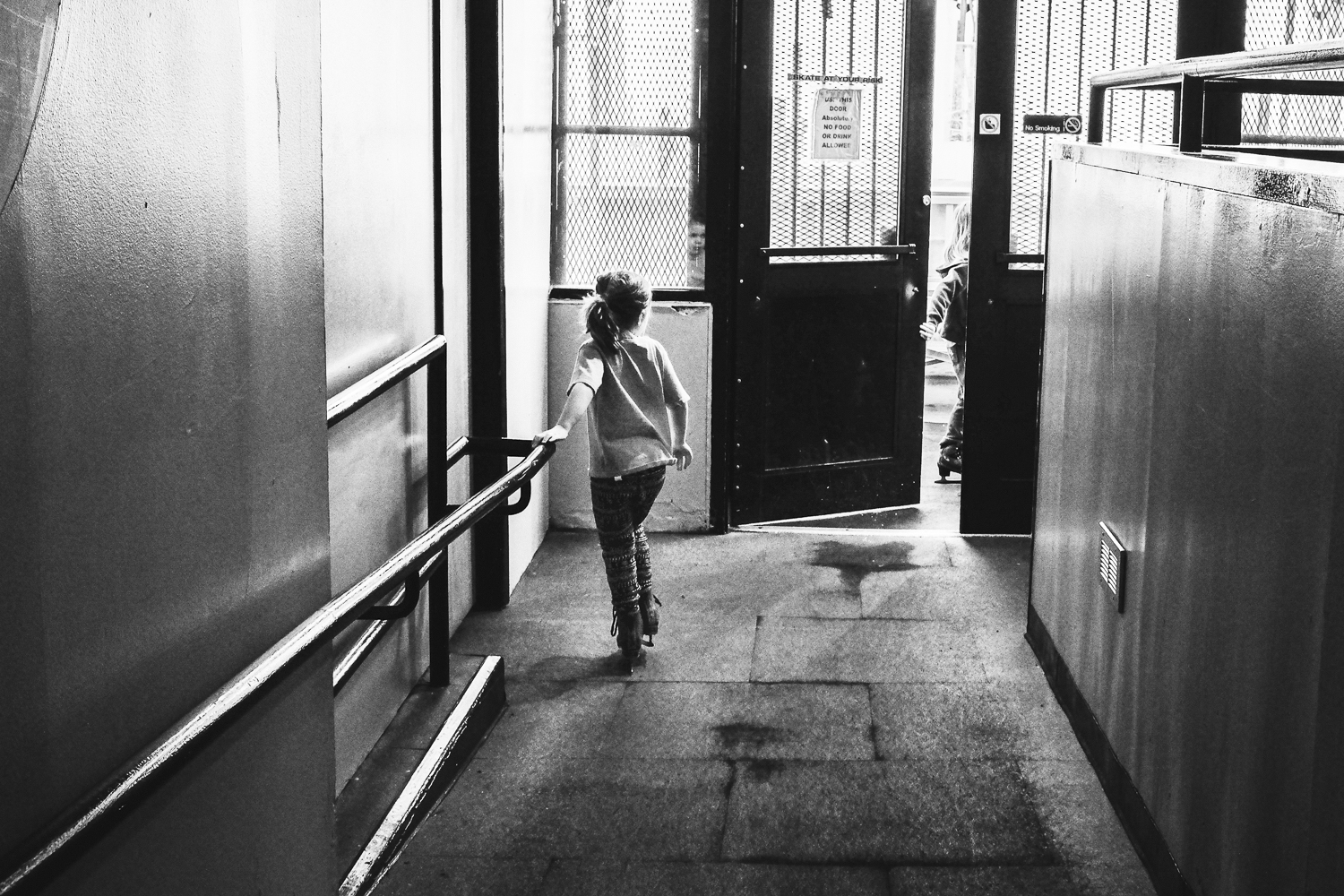 young girl on ice skates for the first time walking towards door to rink