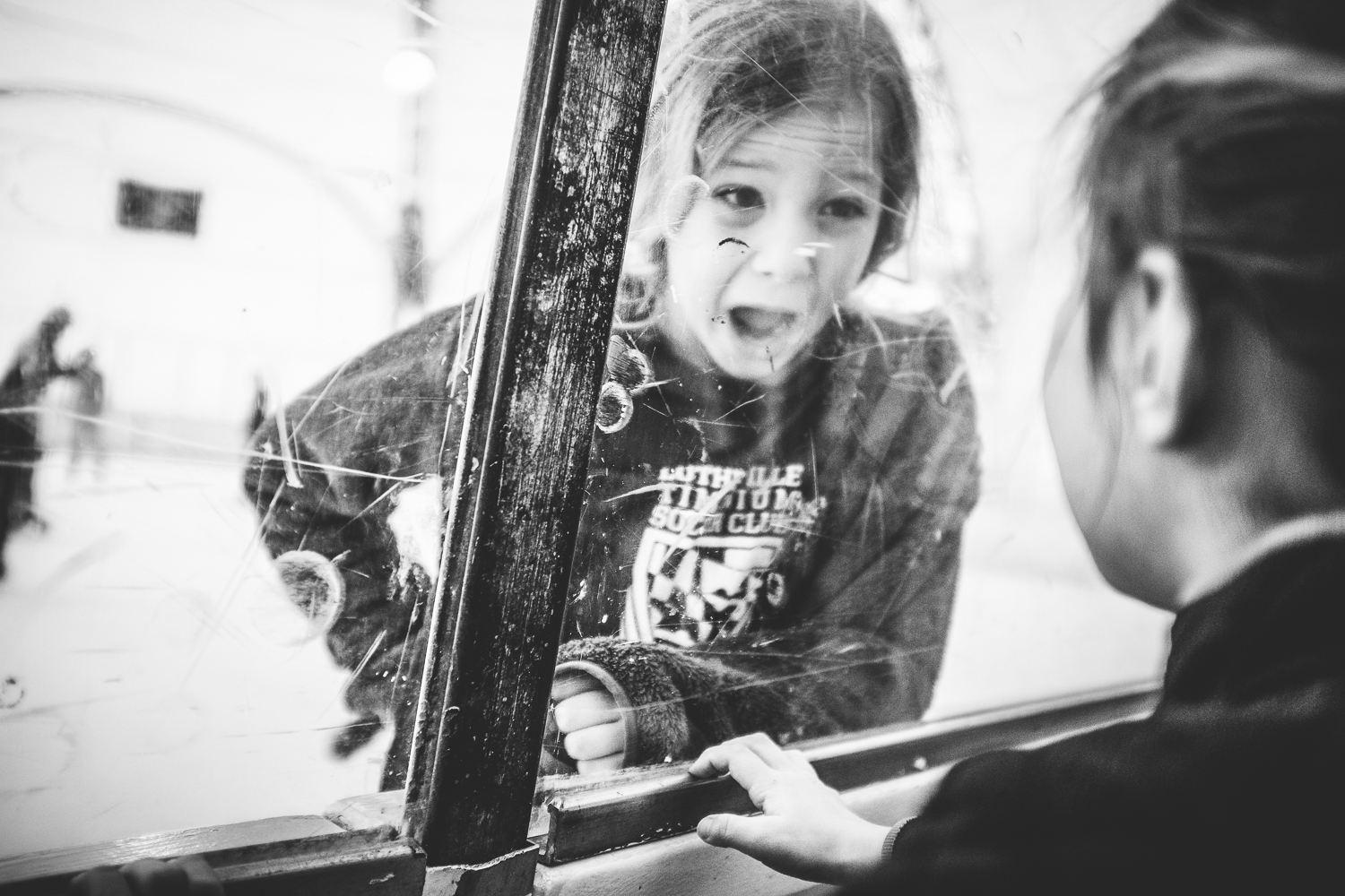 girl smiling at sister through ice rink glass wall.