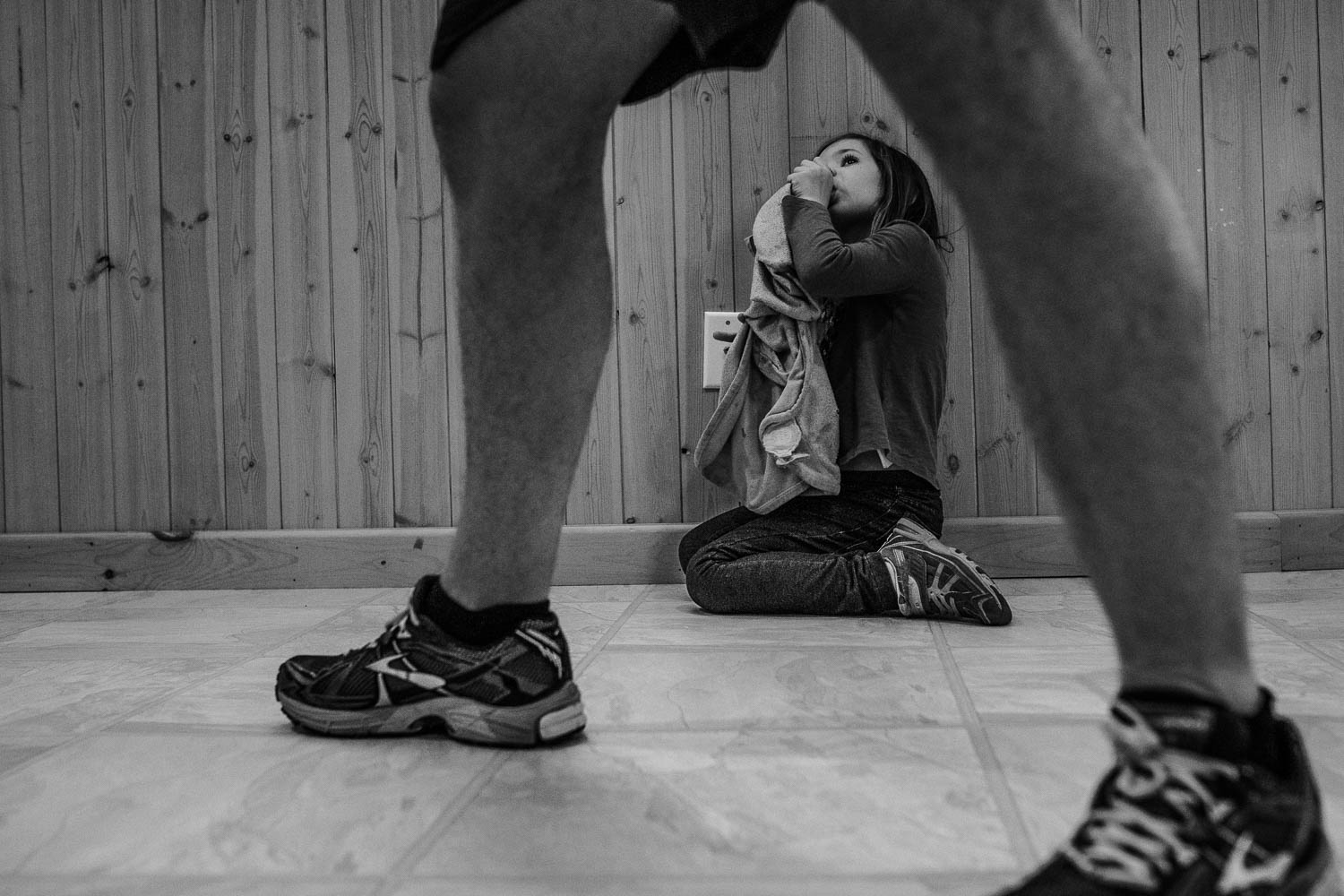 Girl sitting by wall photographed through father's legs.