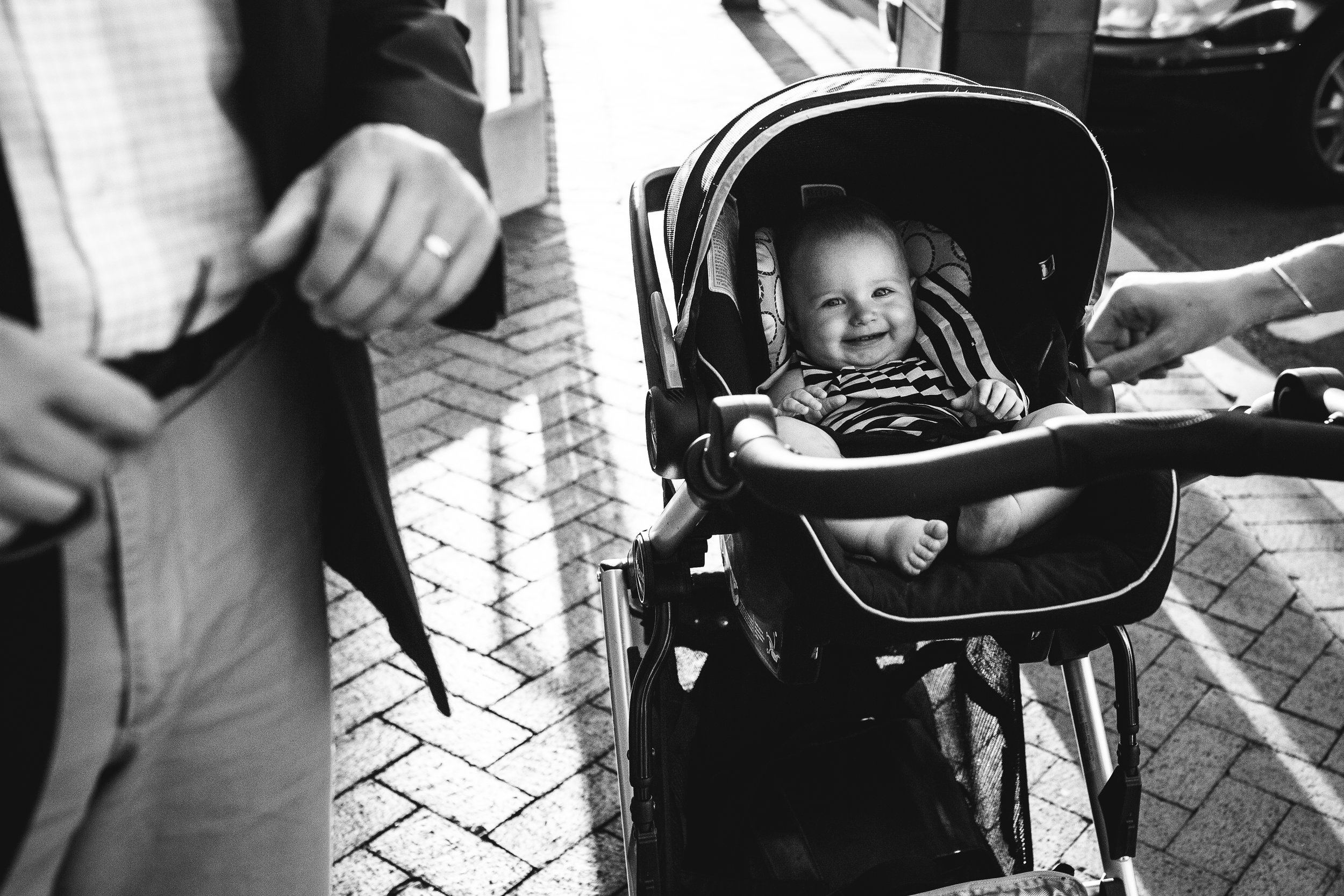 Adorable baby in stroller grinning at camera with parents hands.