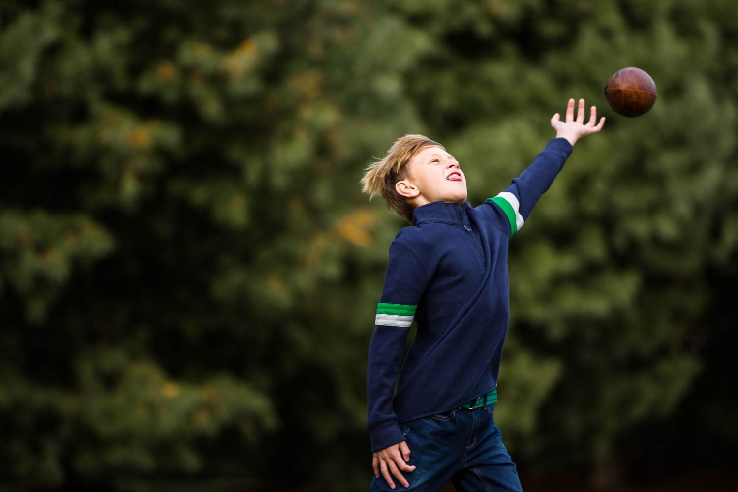  boy in blue sweater reaching to catch ball 