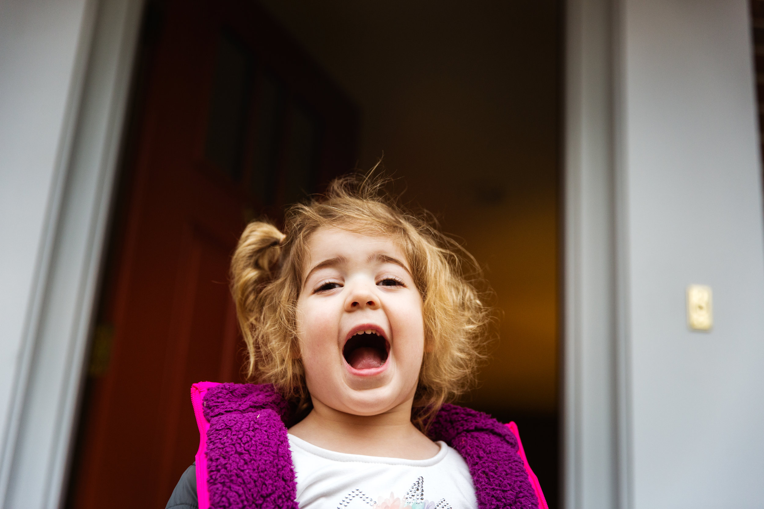 little girl in pink jacket smiles in doorway to her family home