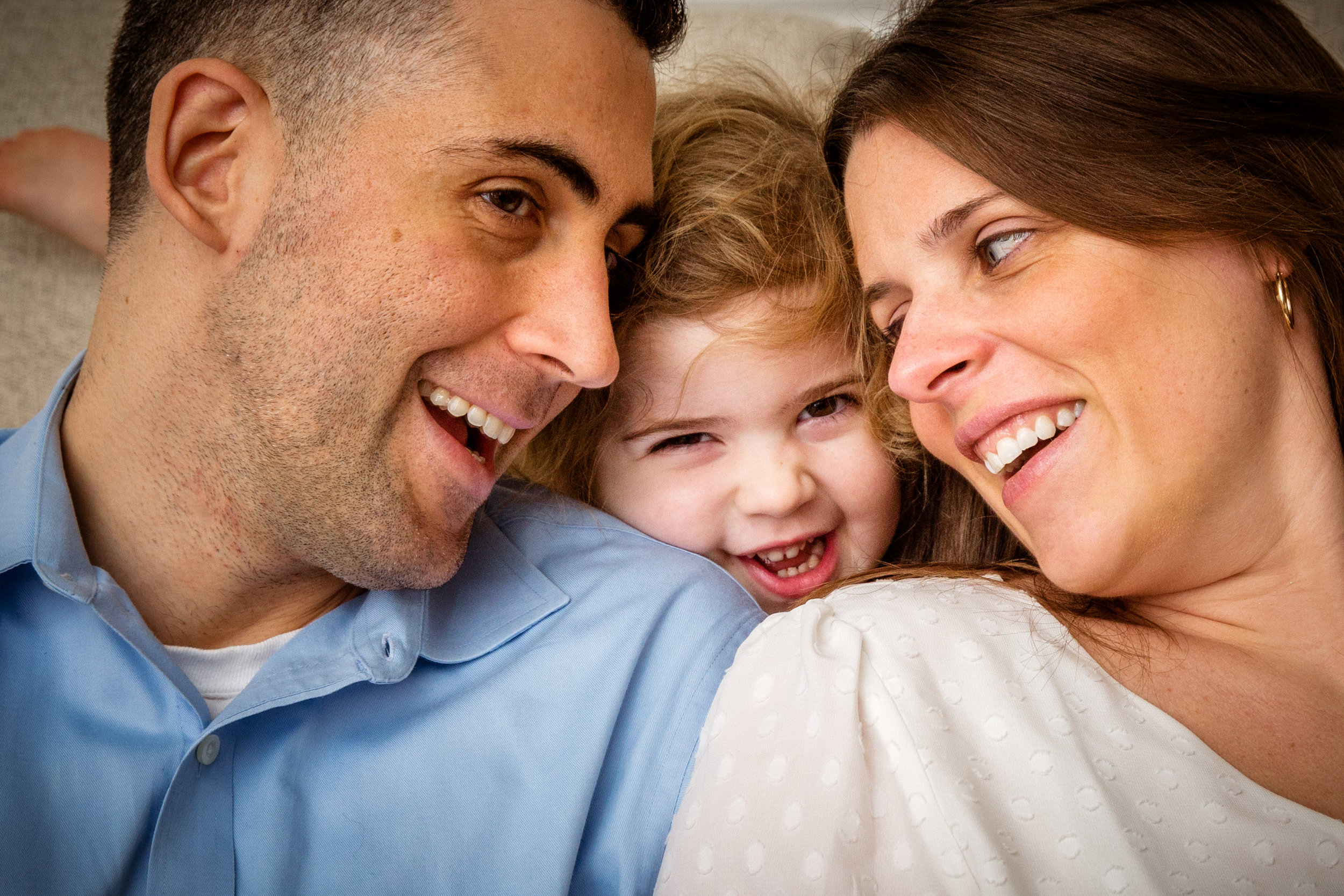 family of three smiles together with cute little girl in between her parents.