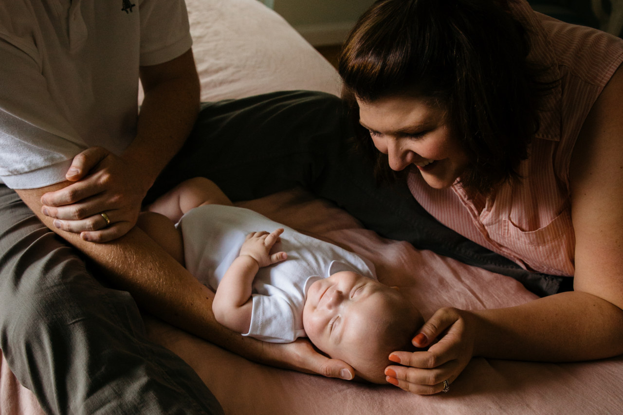parents adore their newborn lying on the bed in gorgeous side light