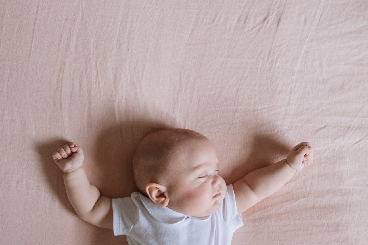 baby boy lying with arms up in crib on pink sheet