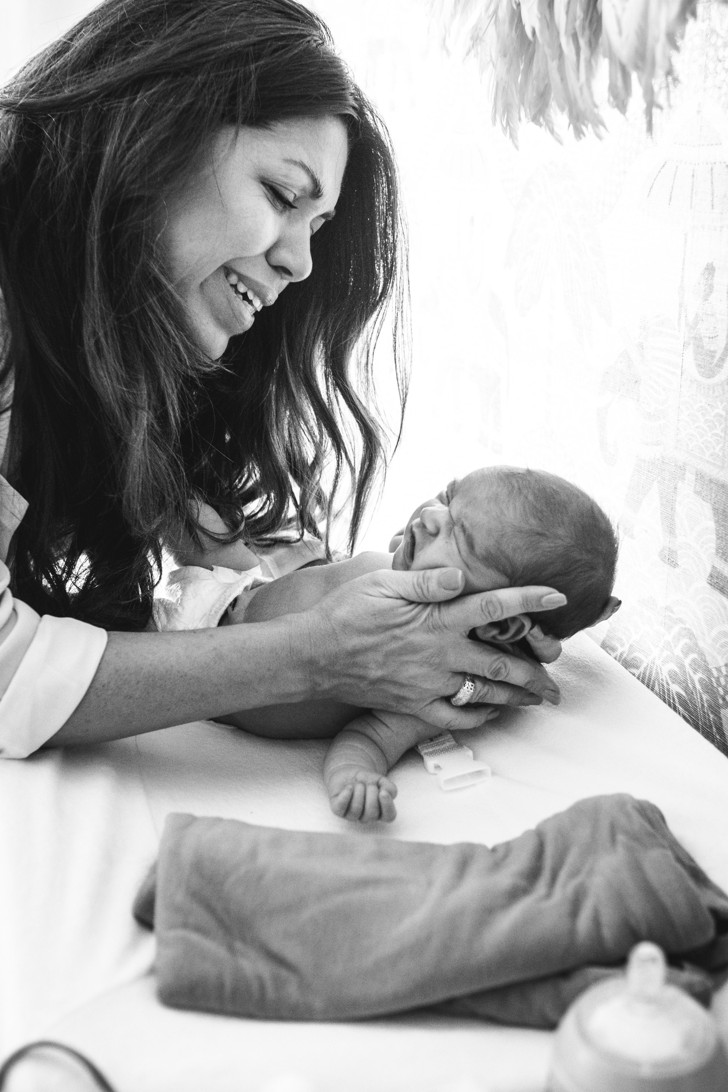 new mother tends to daughter and smiles at her while changing her diaper in black and white photograph