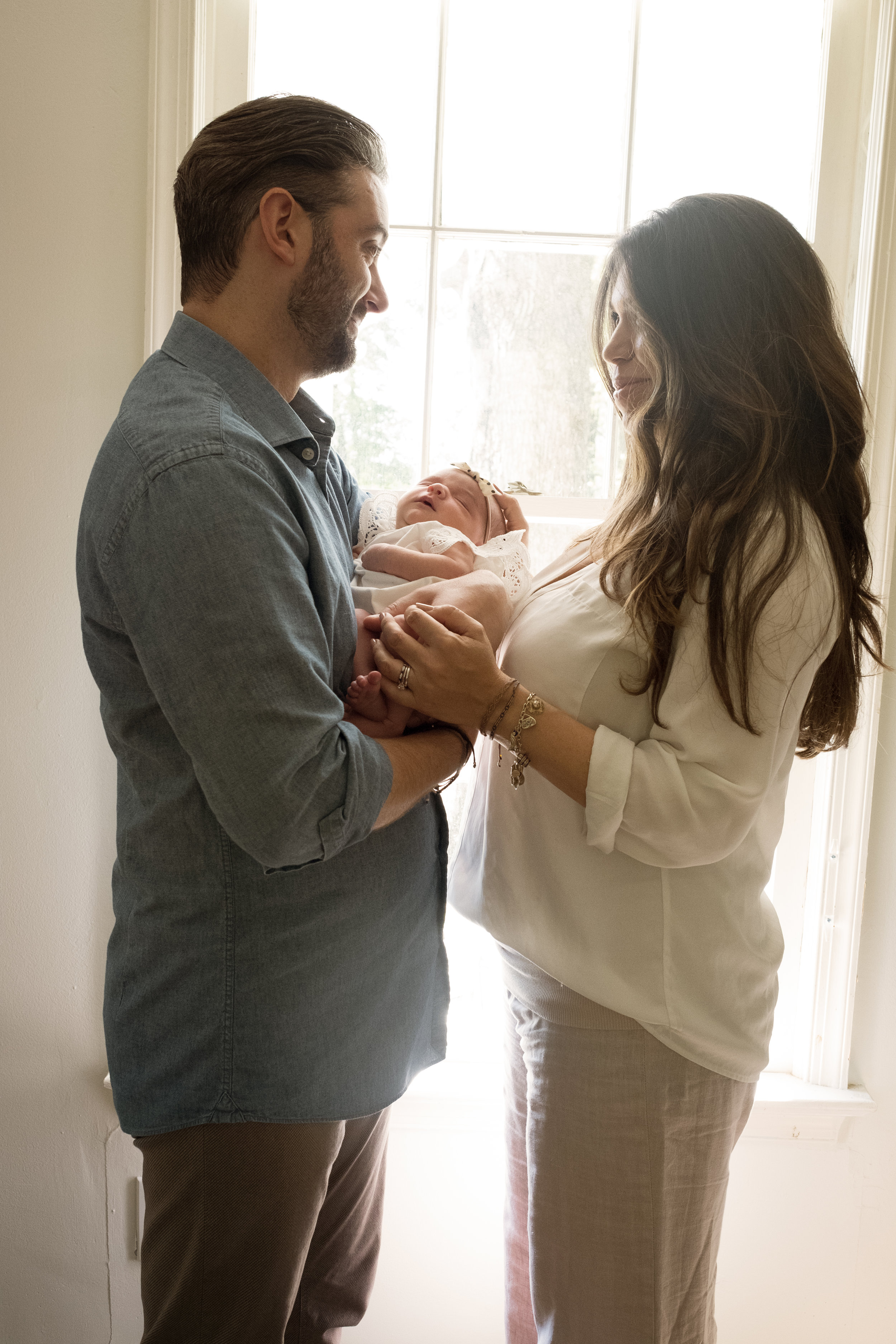 color photograph of new parents facing each other and looking at newborn baby girl