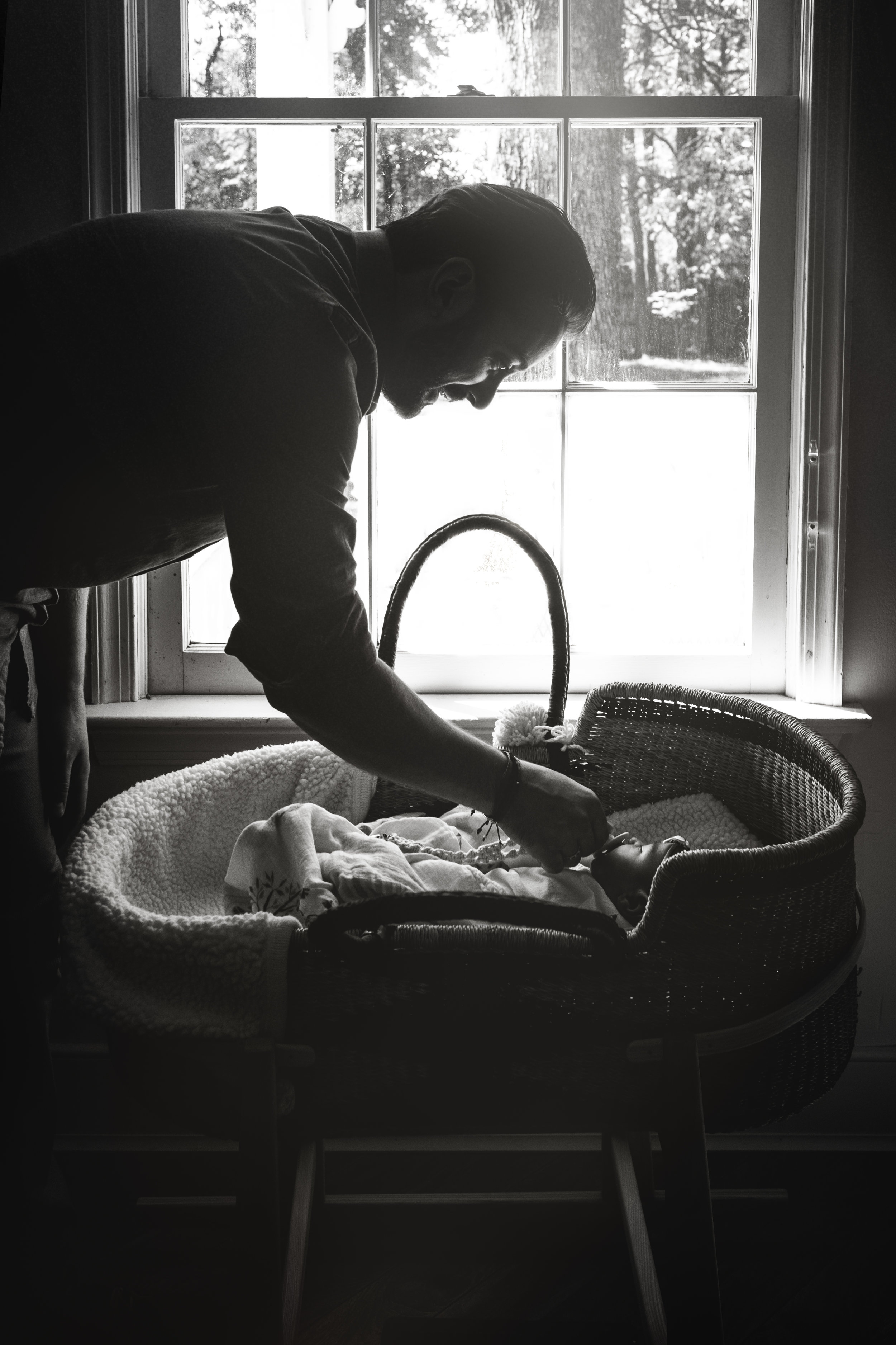 black and white silhouette photograph of father tending to baby daughter in bassinet